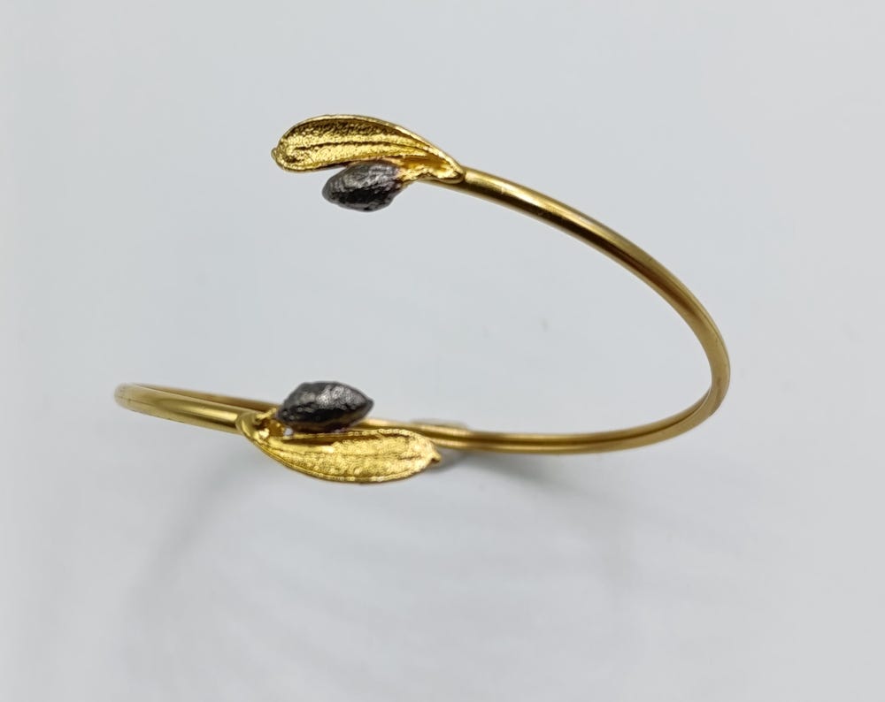 A gold bracelet with leaf-shaped charms and a small black gemstone on a white background.