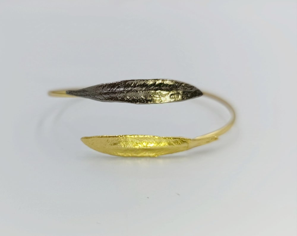 A gold and black bracelet with a leaf-like design, placed on a white background.