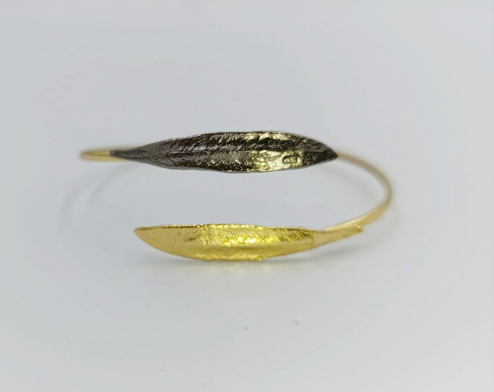 A gold and black bracelet with a leaf-like design, resting on a white surface.