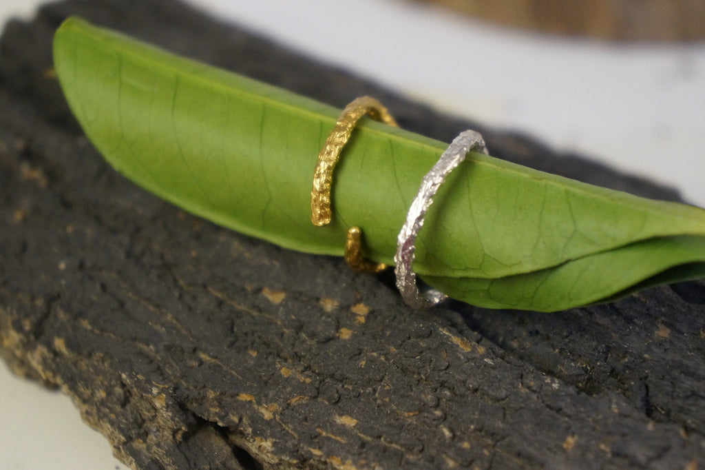 Two rings, one gold and one silver, are resting on a green leaf.