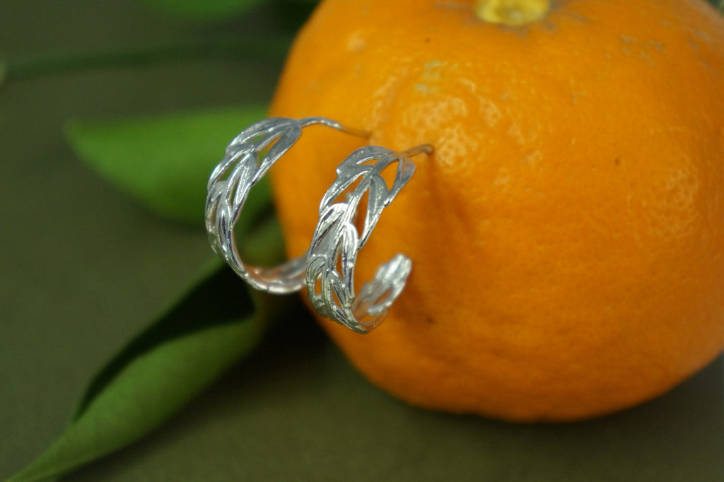 A pair of silver earrings with leaf-like designs rests on top of an orange.