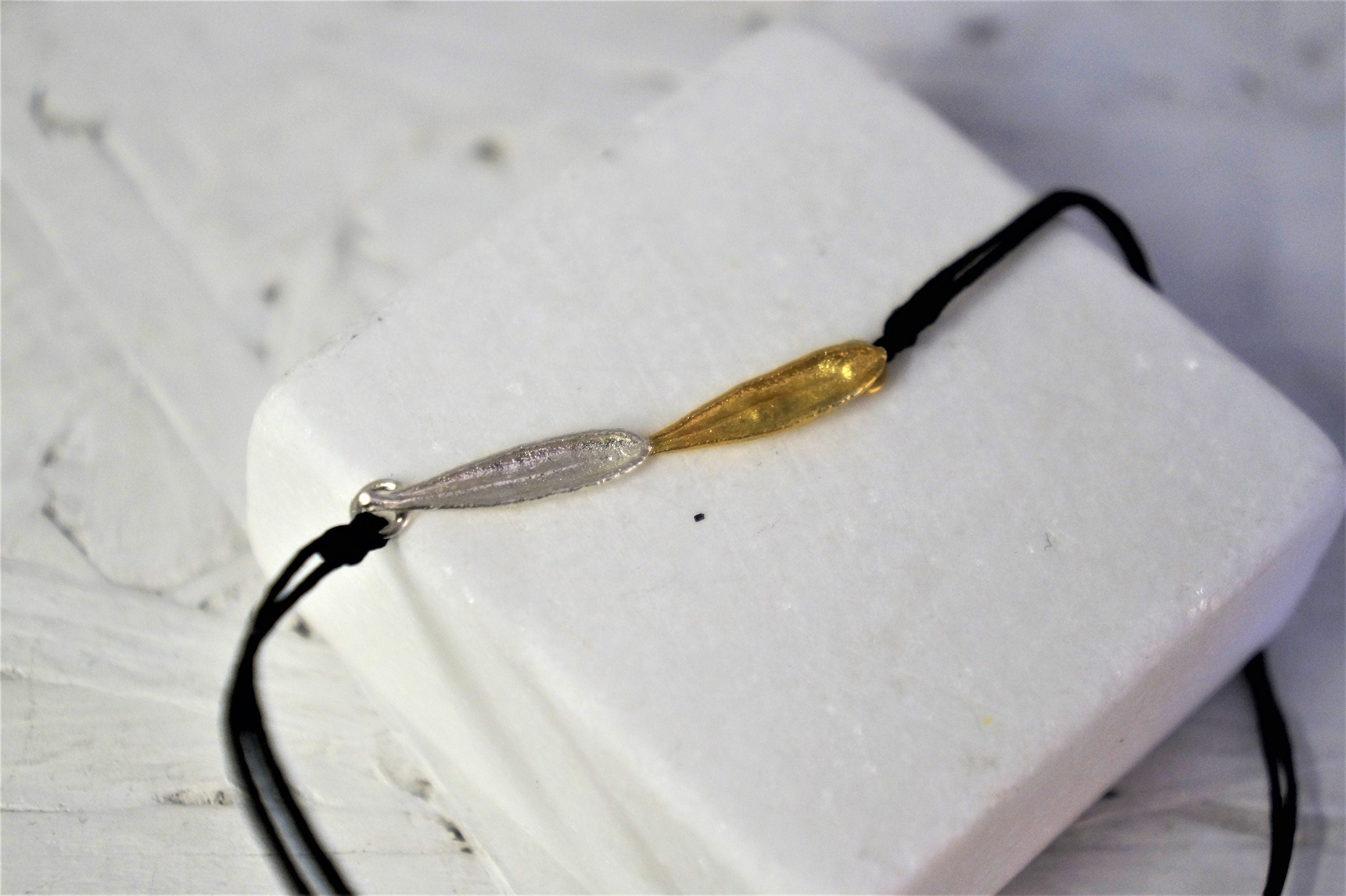 A white square object with a black cord attached to it, featuring a gold-colored leaf-shaped charm.