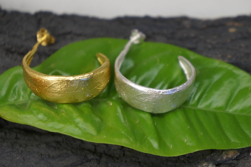 Two earrings, one gold and one silver, are resting on a green leaf.