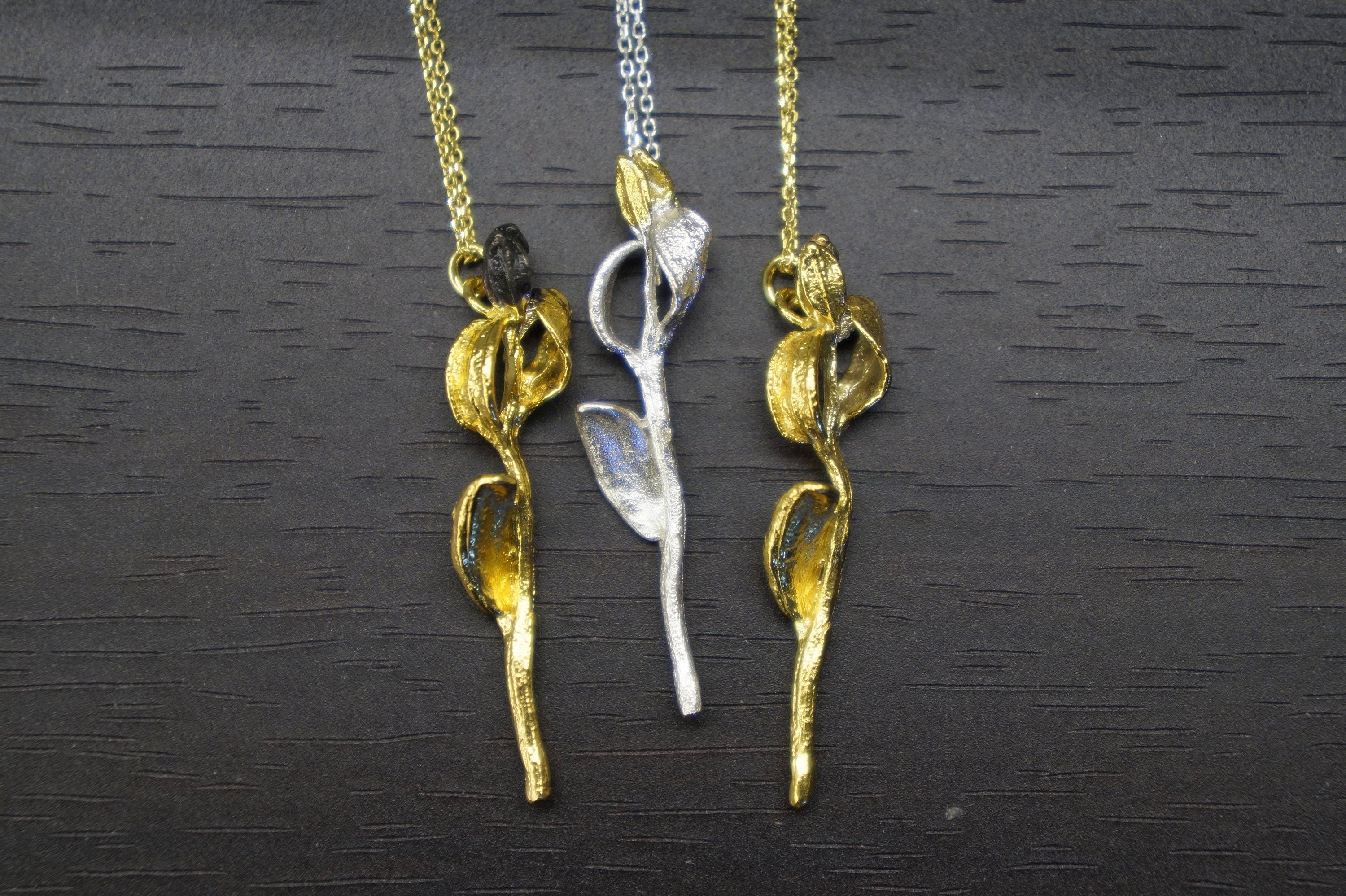 Three gold-colored pendant necklaces with leaf-like designs are displayed on a dark wooden surface.