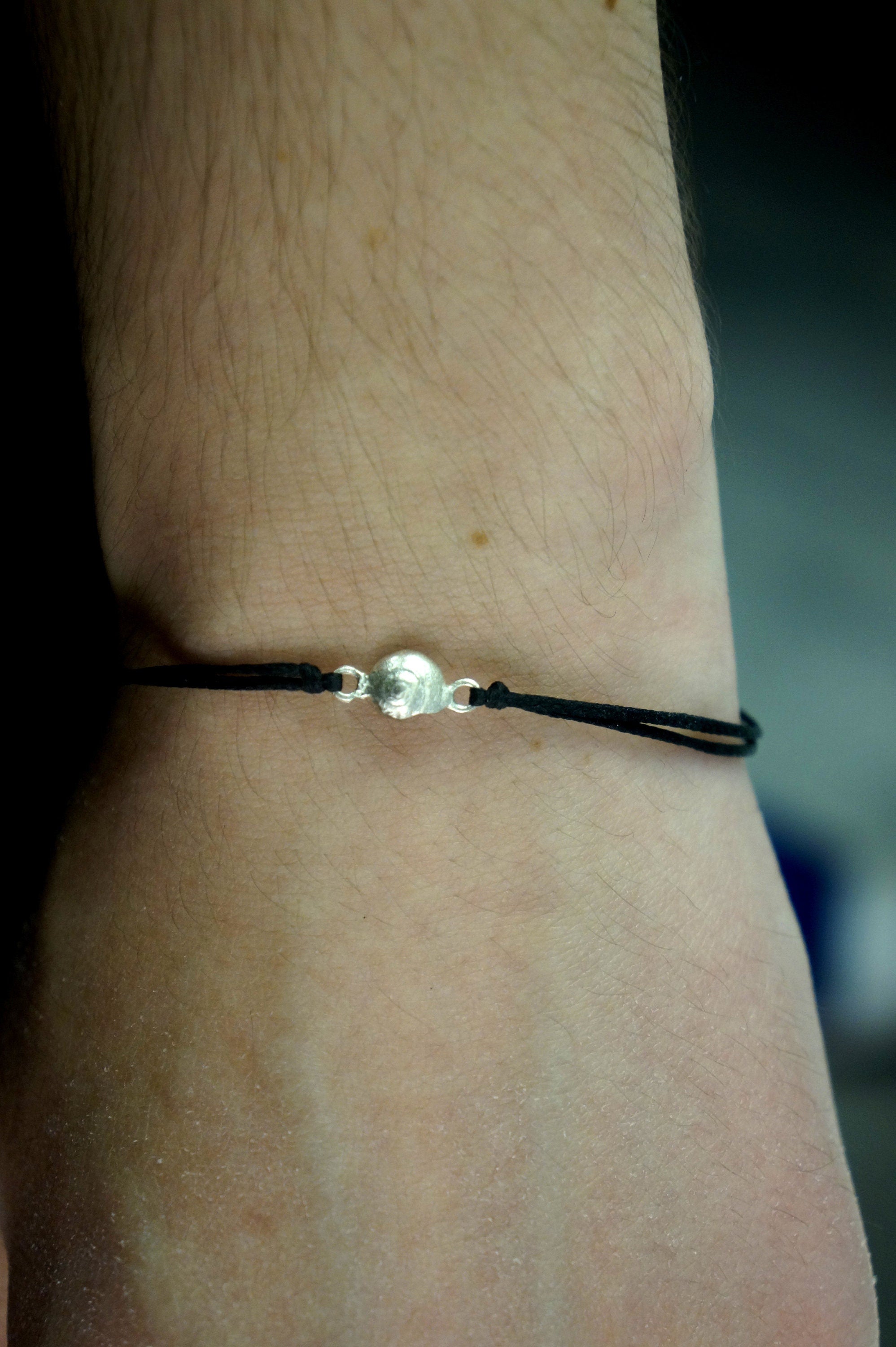 A silver bracelet with a round charm is worn on a person's wrist.
