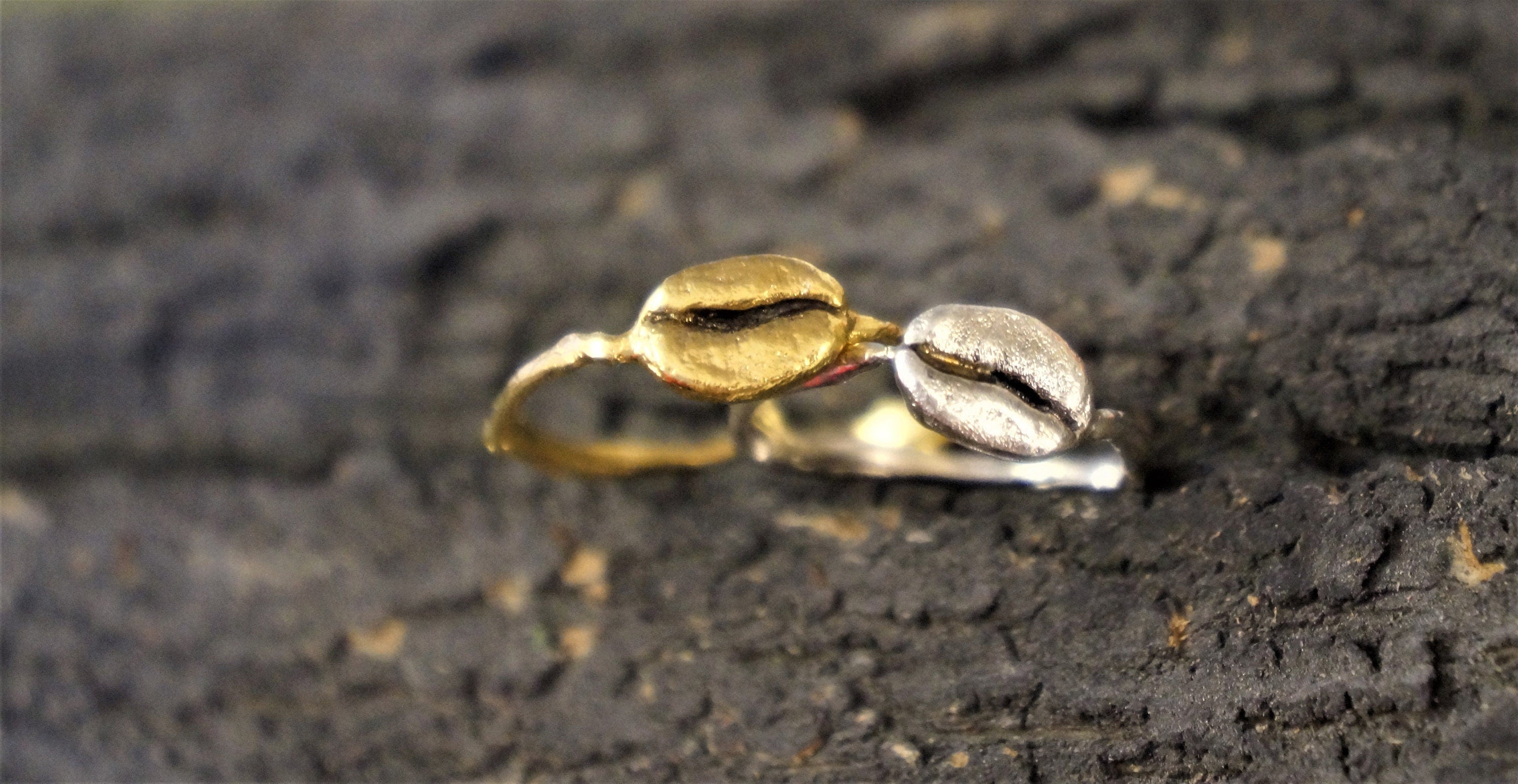 Two rings, one gold and one silver, are placed on a dark, textured surface.
