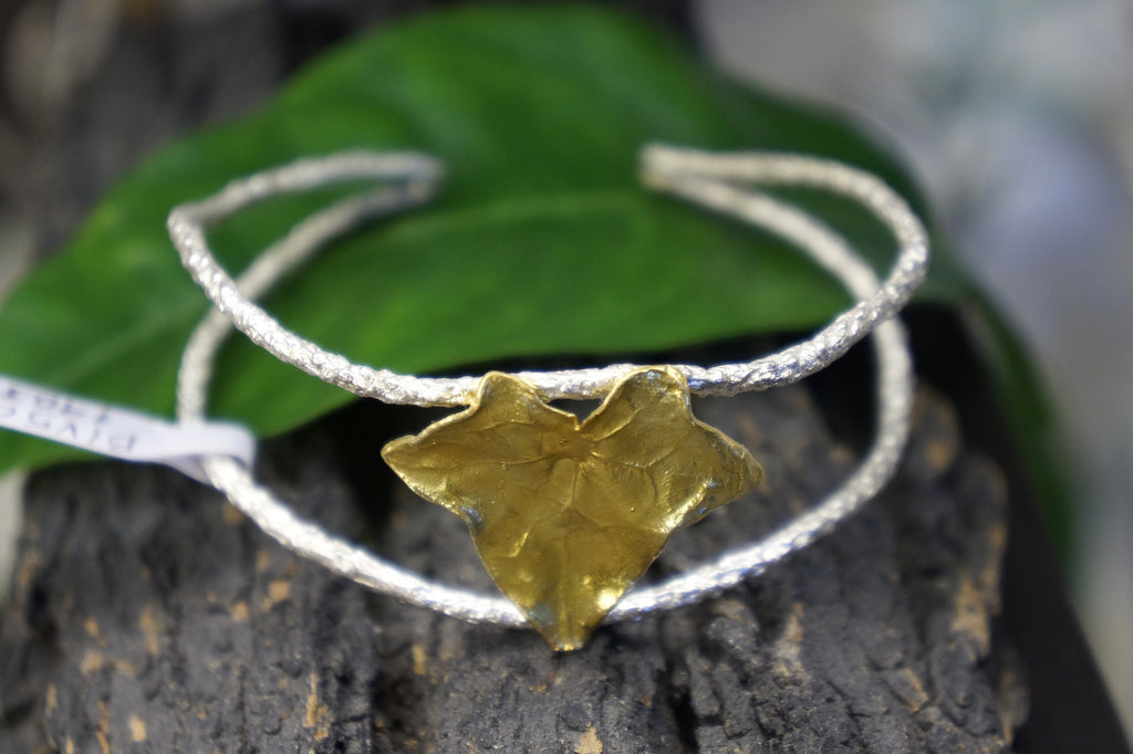A bracelet with a leaf-shaped charm is displayed on a leaf-like surface.