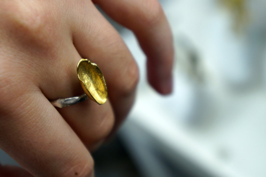 A close-up of a person's hand wearing a gold ring with a unique, oval-shaped design.