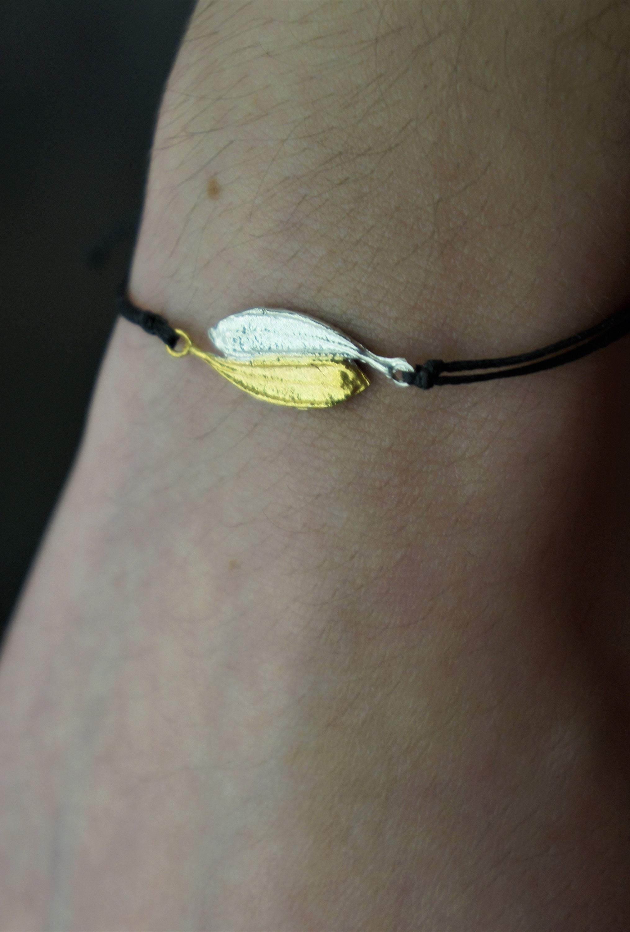 A bracelet with a silver leaf charm on a black cord.
