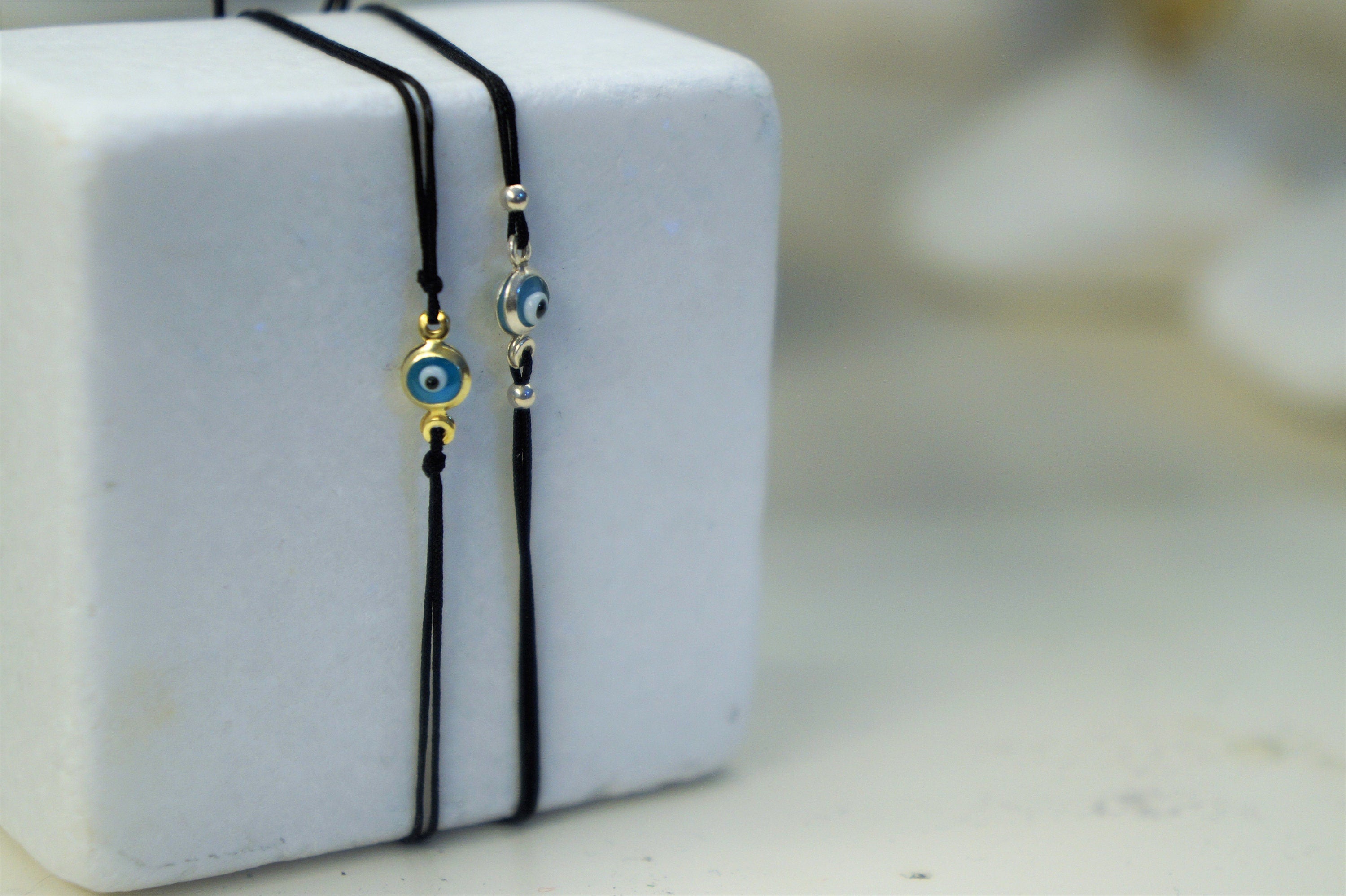 A white square box with two black strings attached to it, each string holding a small, round, blue-colored charm with an eye design.