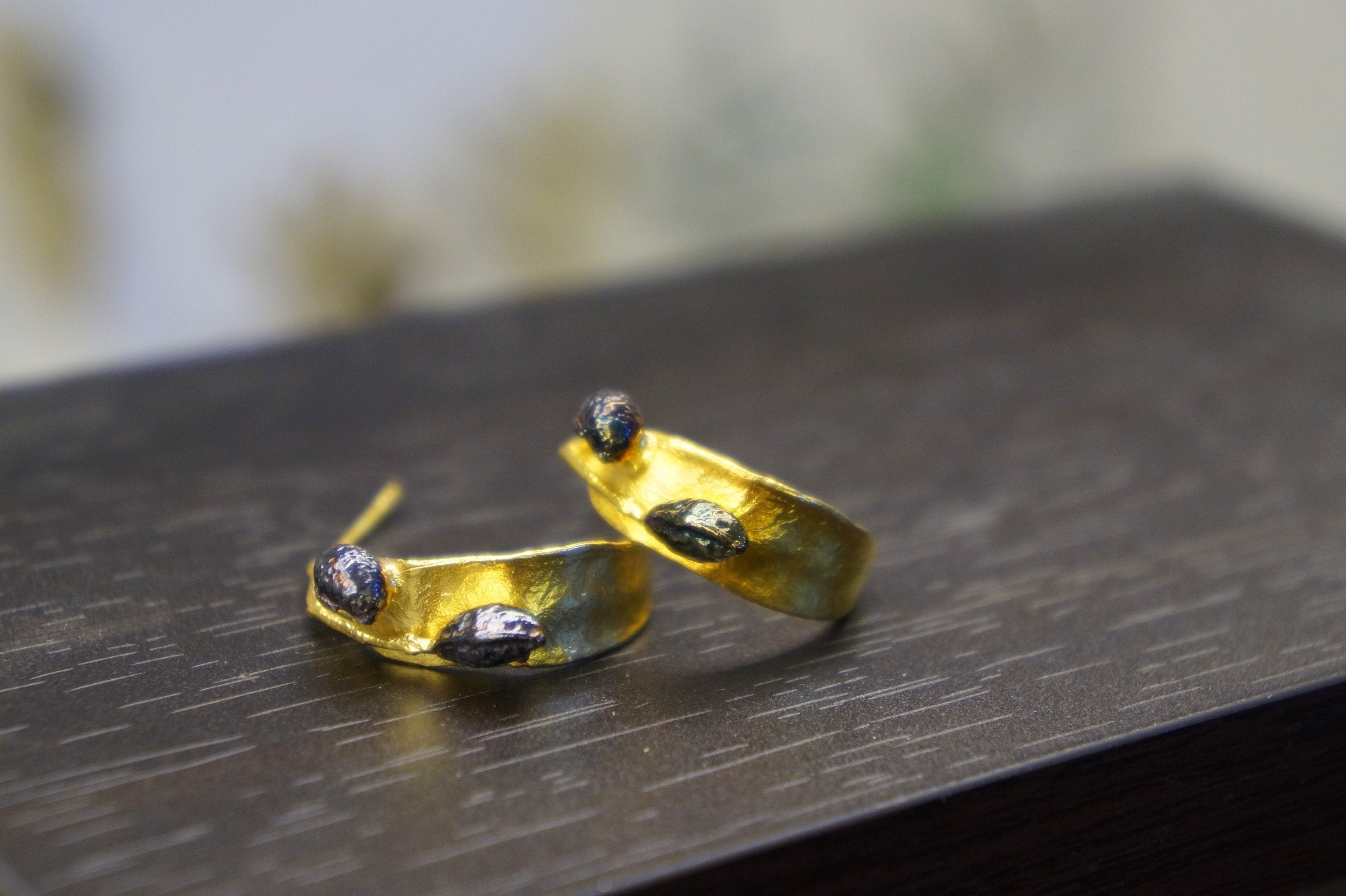 A pair of gold earrings with small stones on the ends, resting on a dark wooden surface.