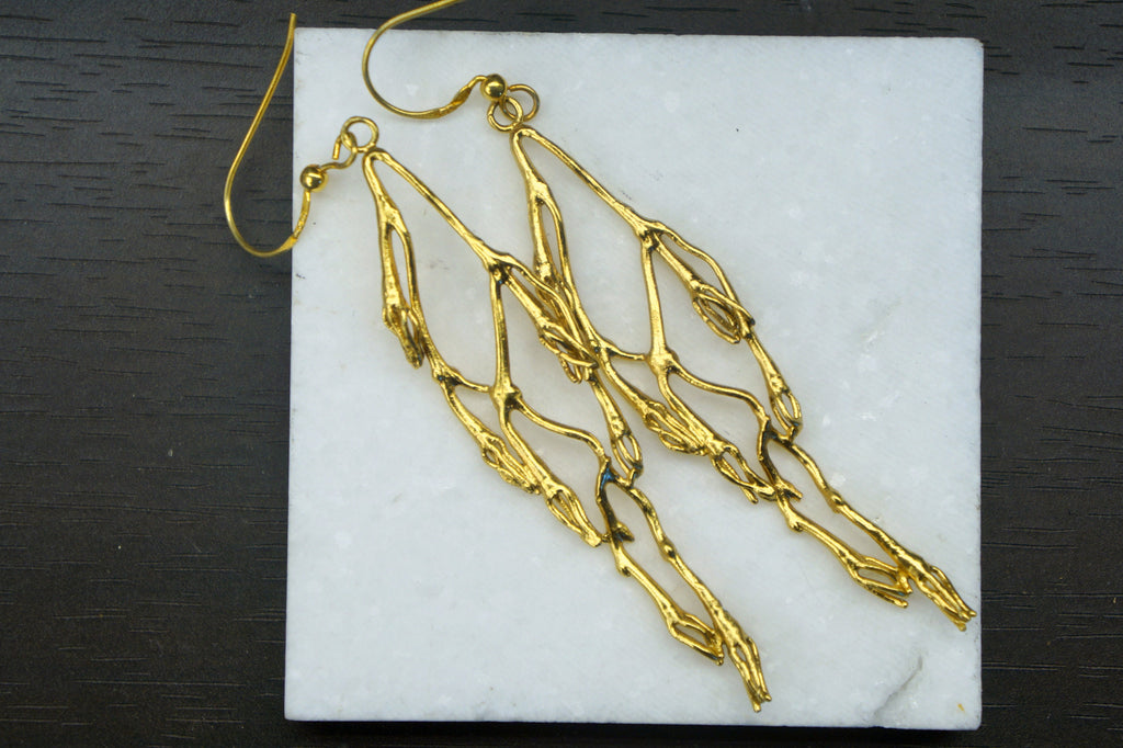 A pair of gold earrings with intricate, organic designs resting on a white marble surface.