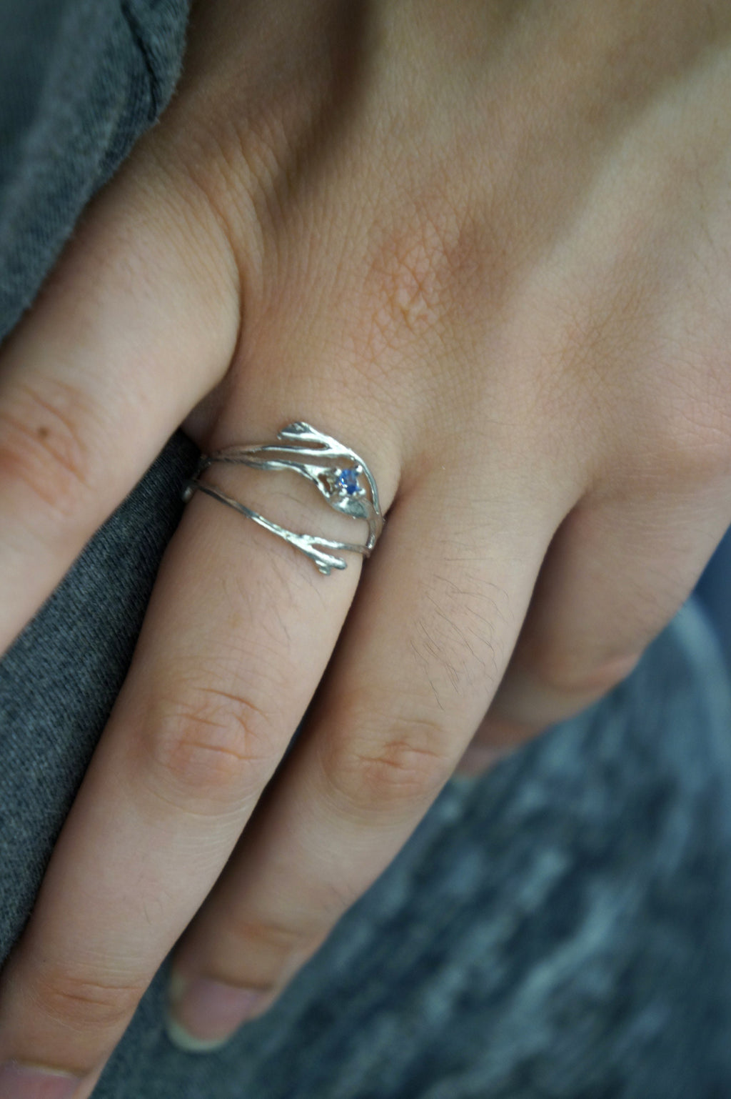A close-up of a person's hand wearing a silver ring with a blue gemstone.