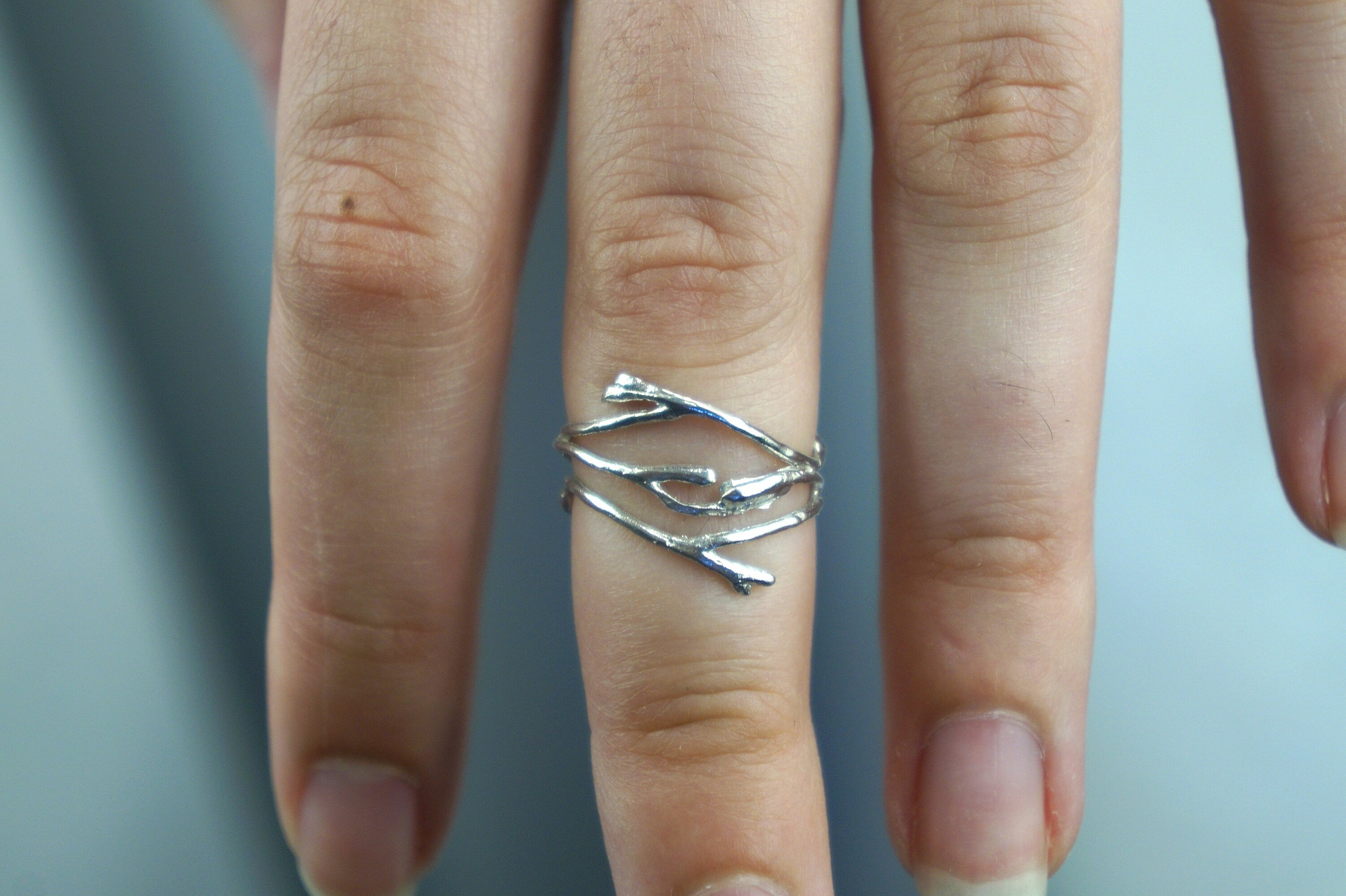 A close-up view of a person's hand wearing a silver ring with a unique design of three intertwined branches.