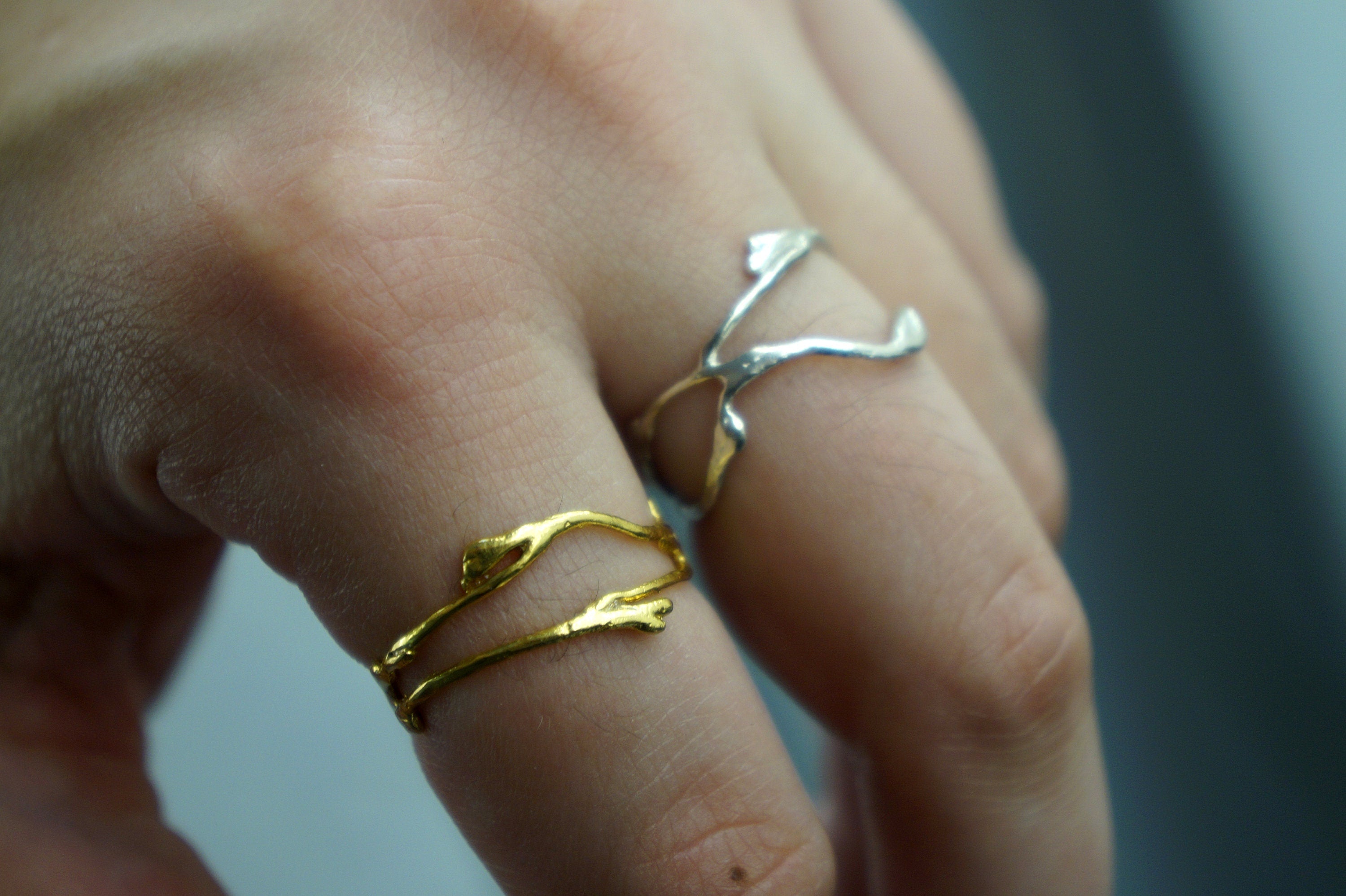 A close-up of a person's hand wearing two rings, one gold and one silver, with the gold ring featuring a leaf-like design.