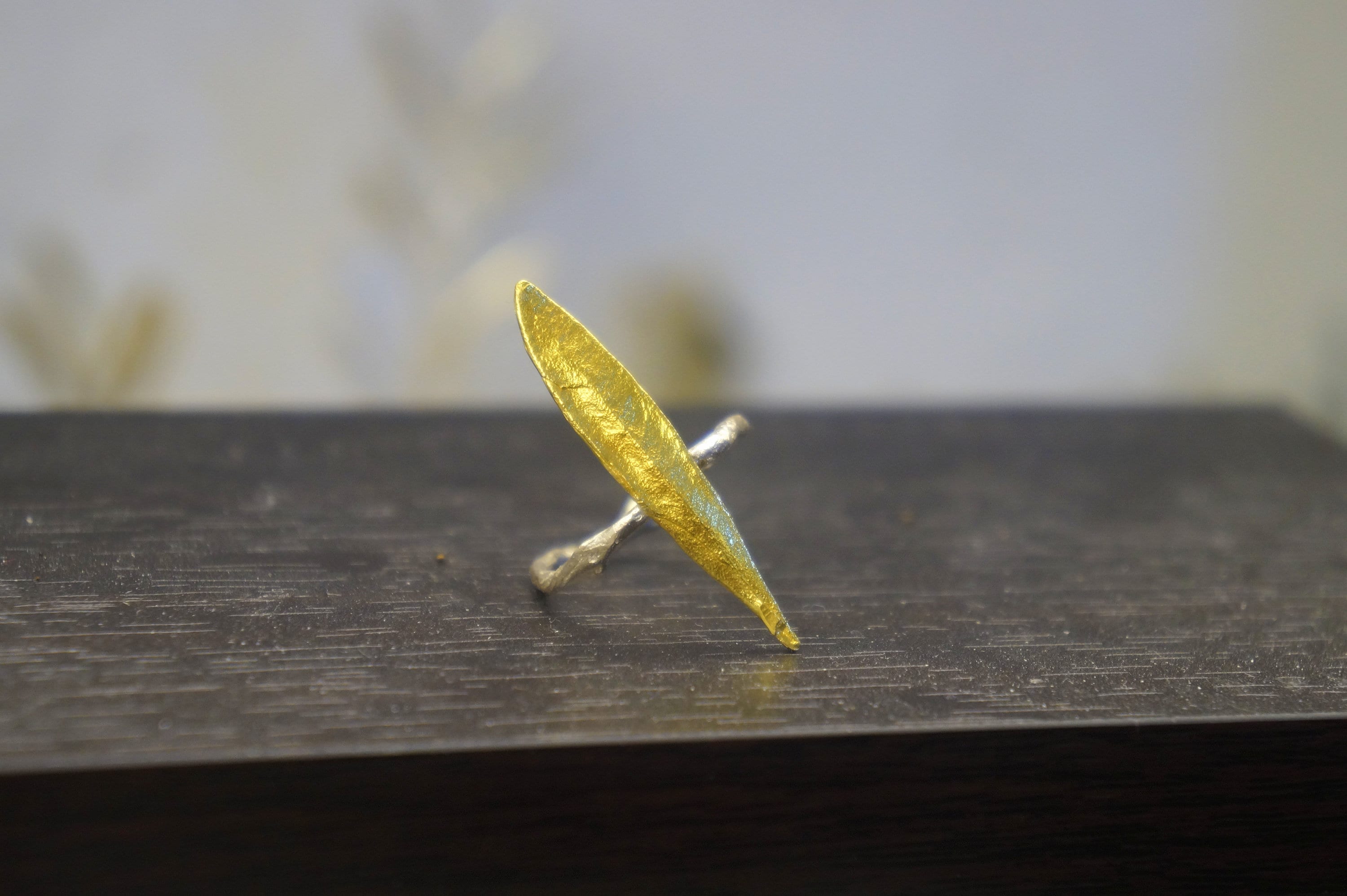 A gold leaf ring with a pointed shape sits on a dark surface.