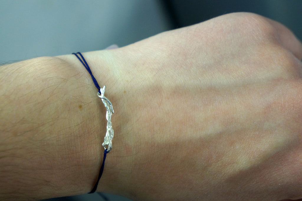 A close-up view of a person's wrist wearing a blue bracelet with a silver charm.