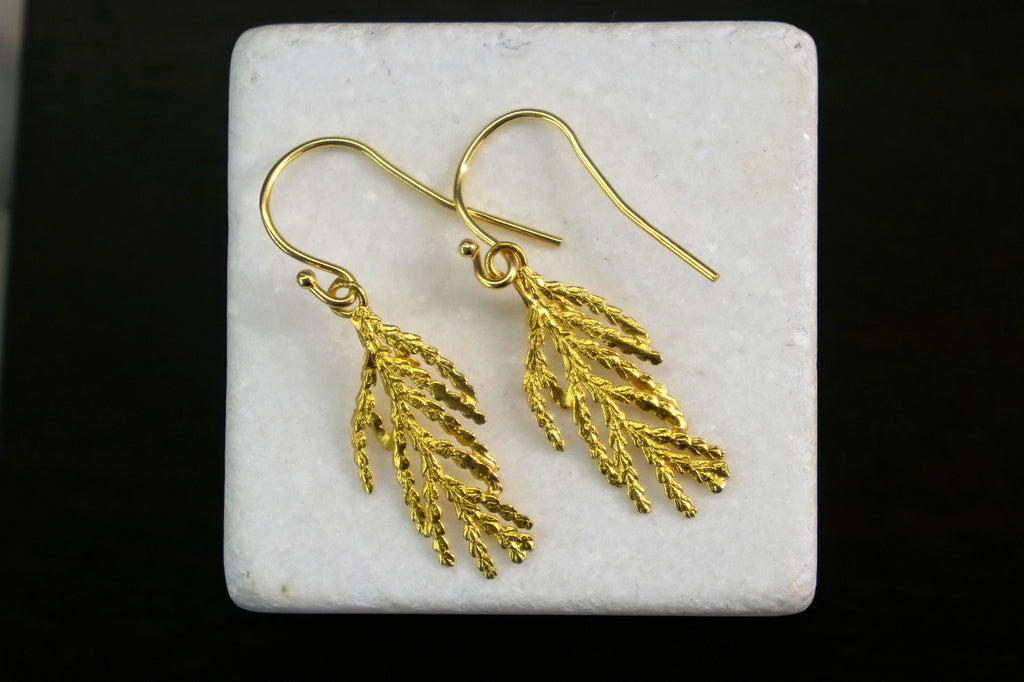 A pair of gold earrings with leaf-like designs, displayed on a white surface against a black background.