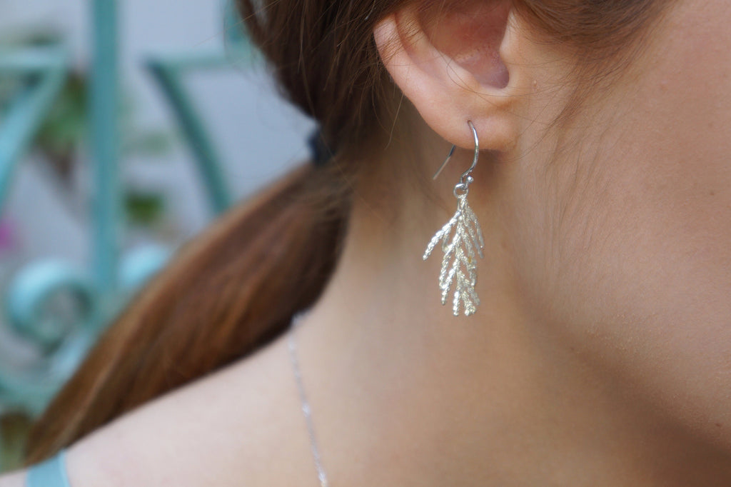 A close-up view of a person's ear wearing a delicate silver earring with a leaf-like design.