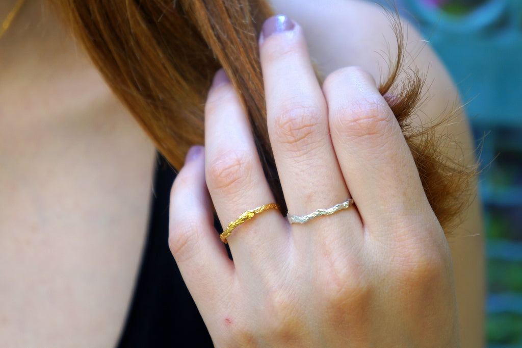 A close-up of a person's hand wearing two rings, one gold and one silver, with their hair visible.