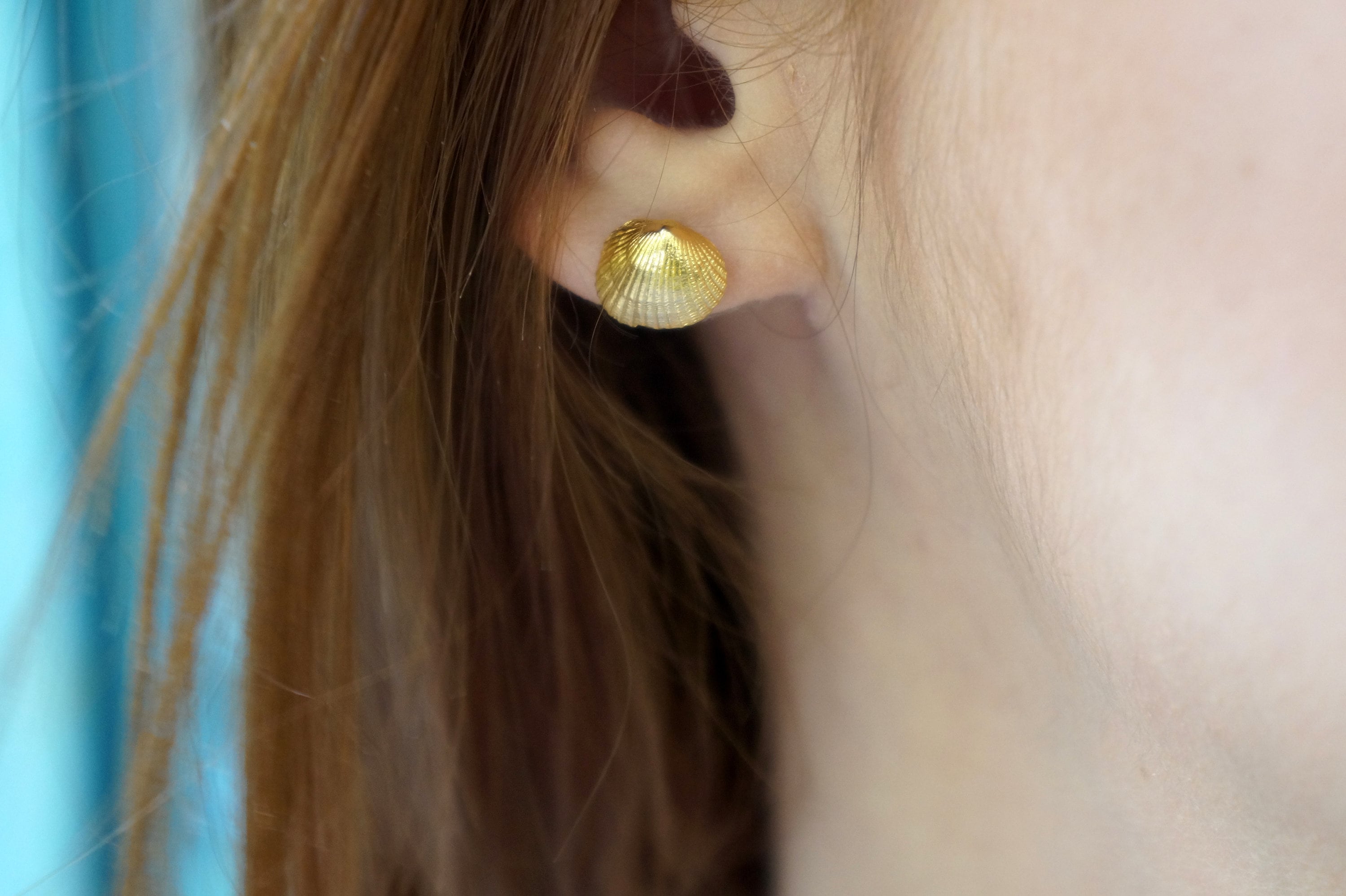 A close-up view of a person's ear with a gold shell earring.