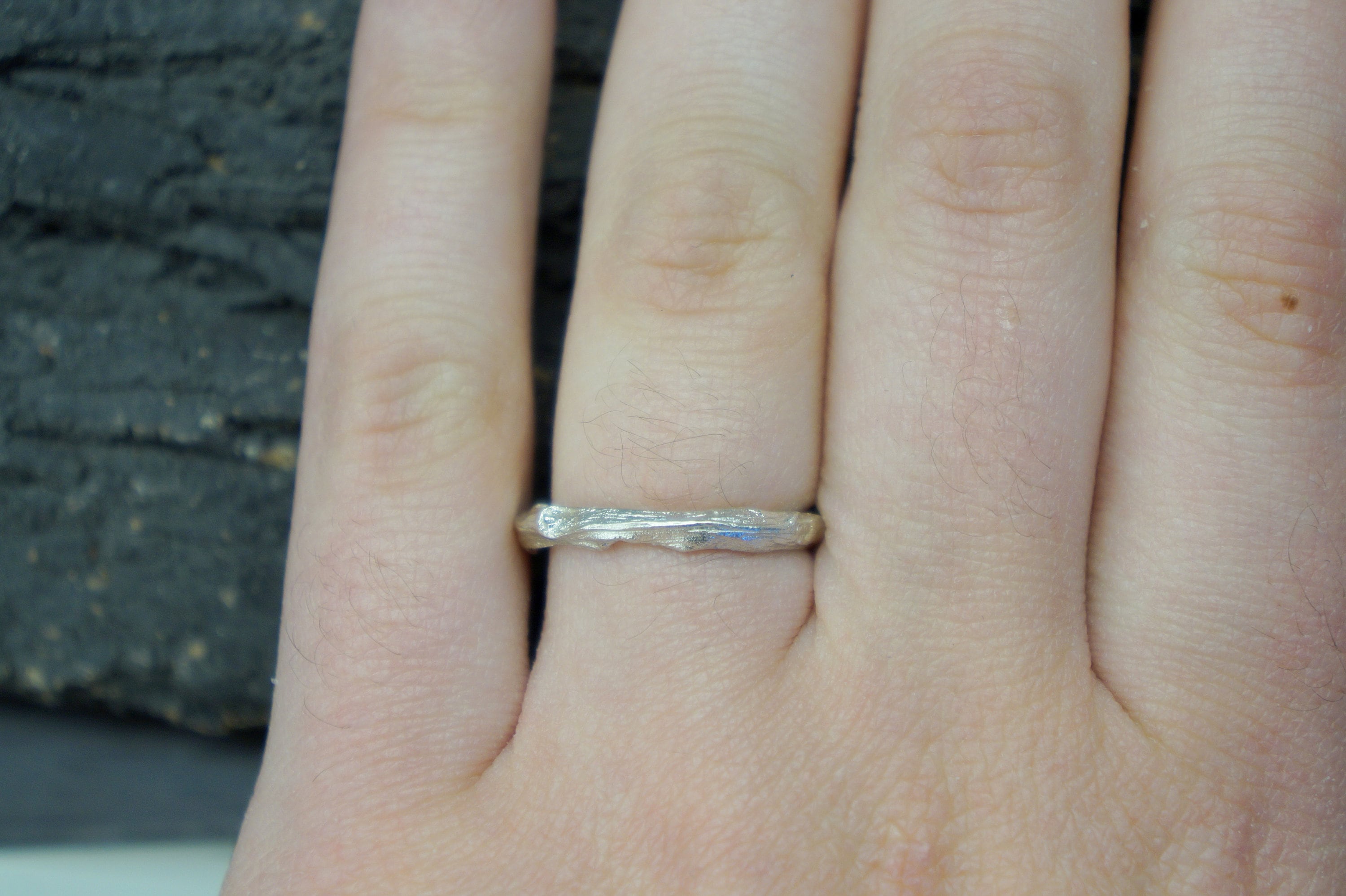 A close-up of a person's hand wearing a silver ring with a unique, tree-like design.