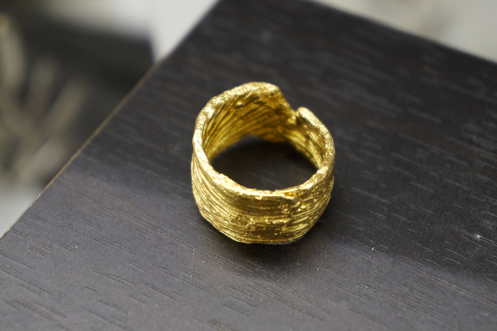 A gold ring with a textured, twisted design sits on a dark surface.