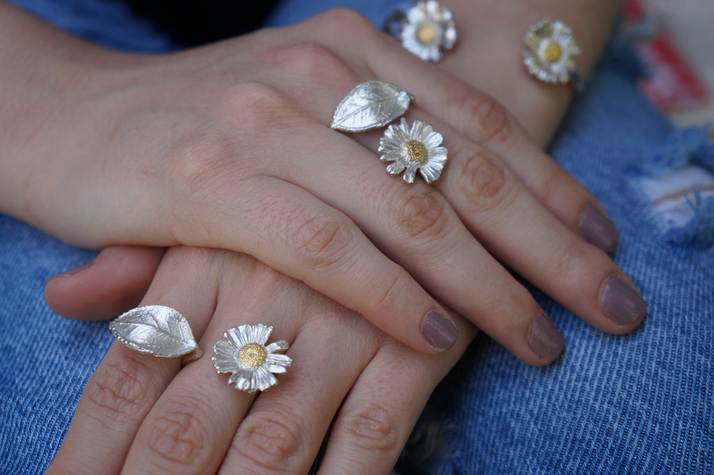 A close-up image of a person's hands wearing multiple rings with silver and gold designs, including leaves and flowers.