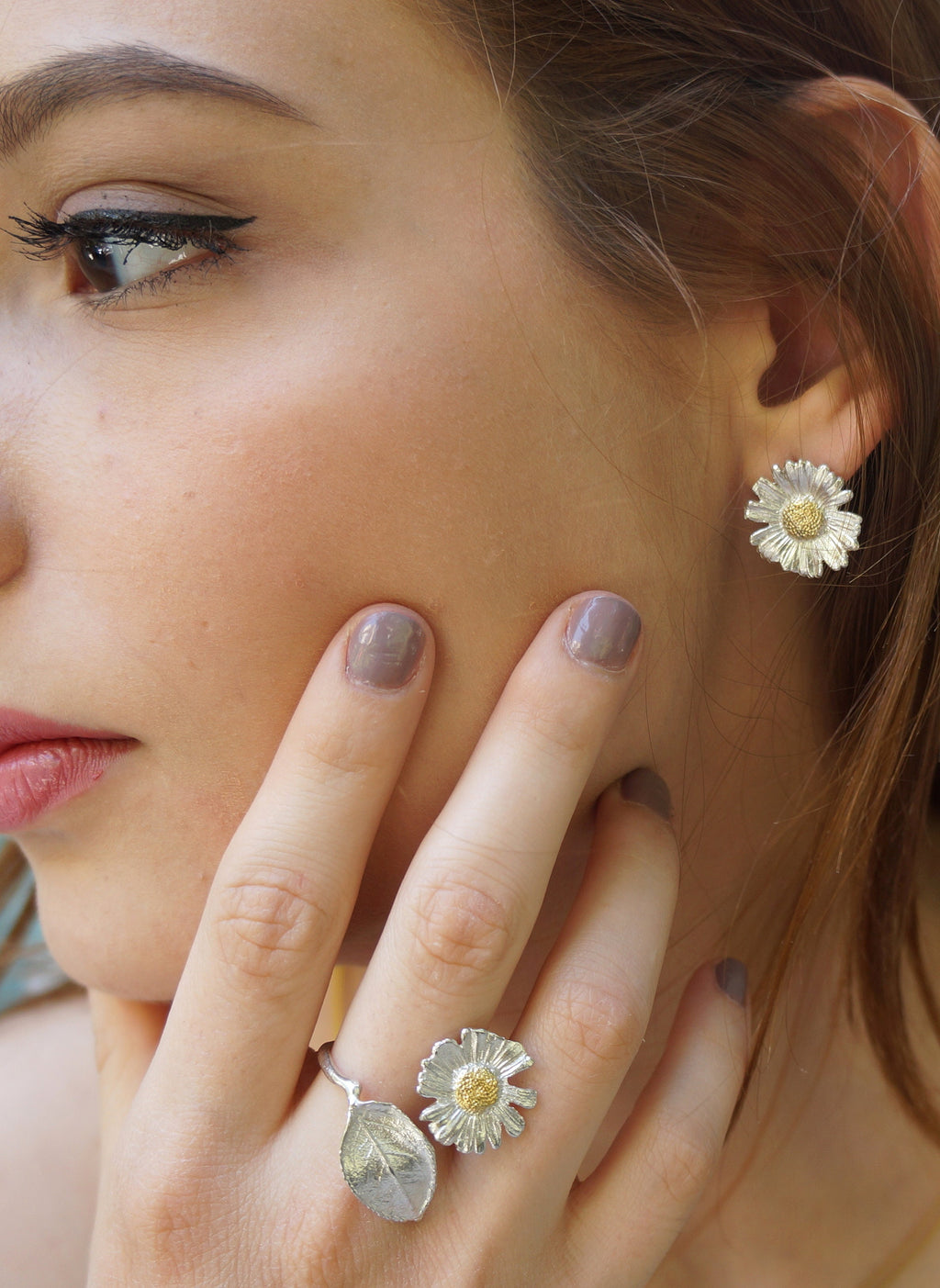 A close-up of a woman's face, focusing on her hand adorned with multiple rings and earrings.