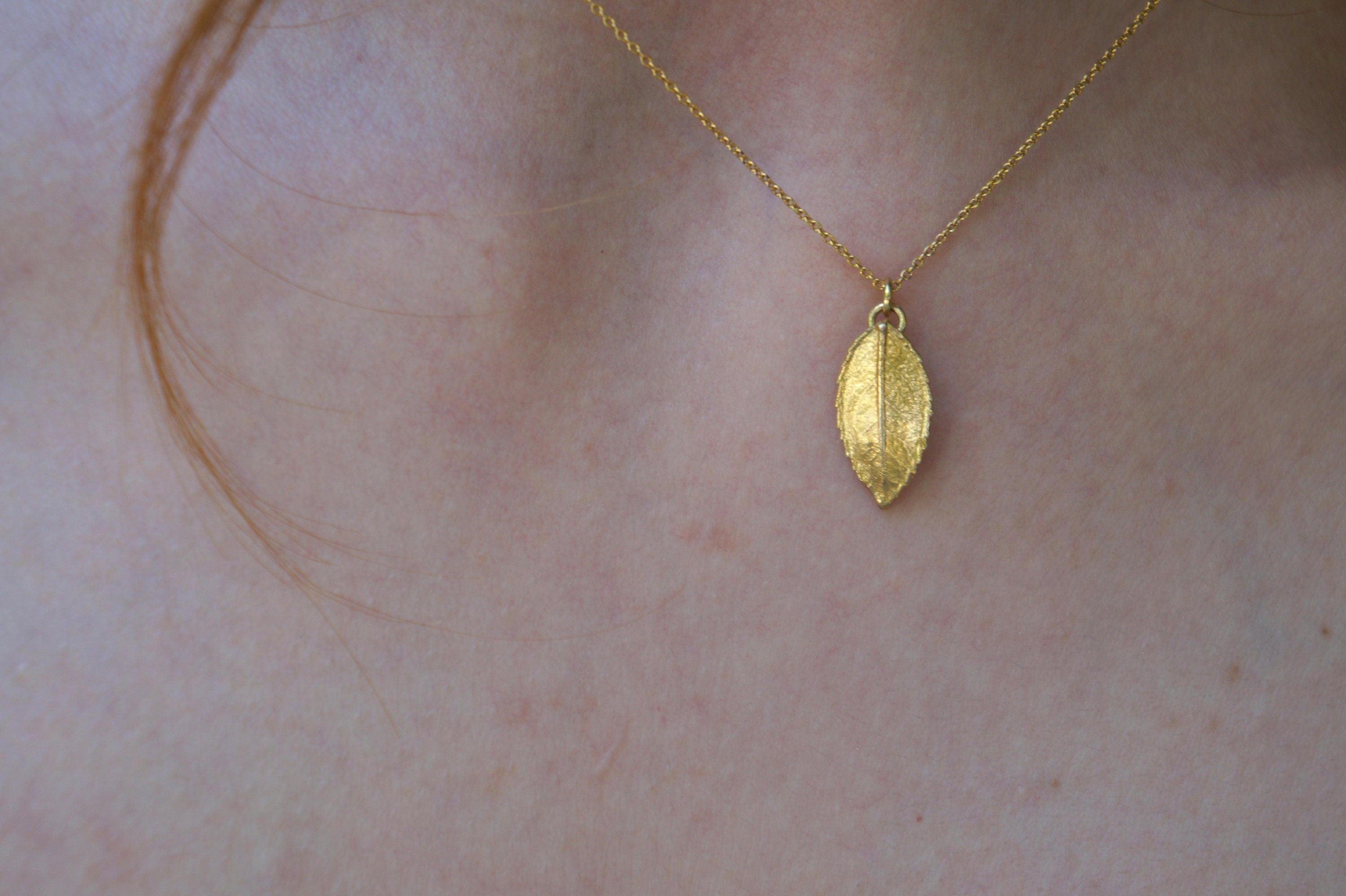 A gold leaf pendant necklace is worn around a person's neck.
