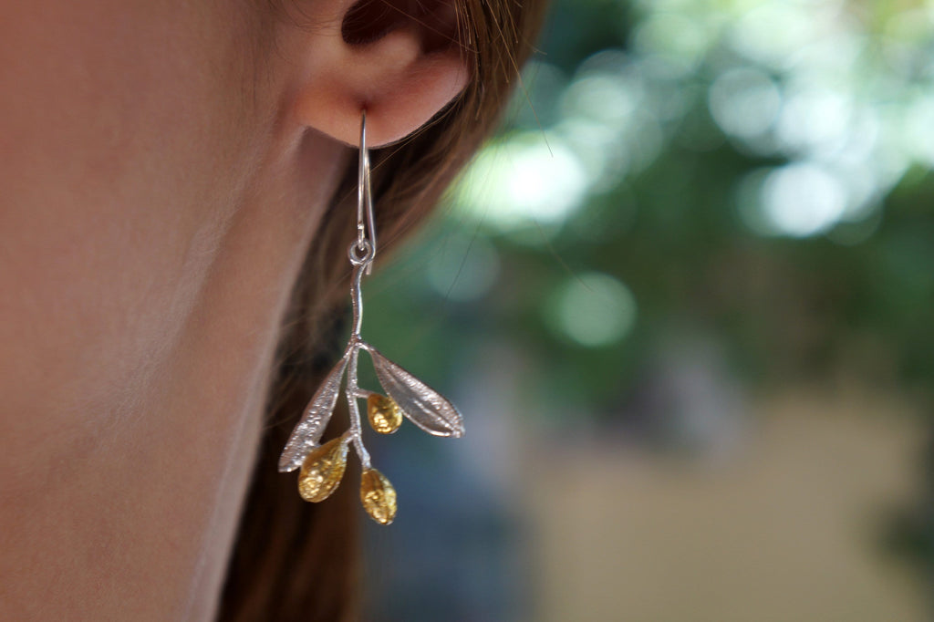 A close-up view of a person's ear wearing a pair of earrings with a branch-like design and small golden leaves.