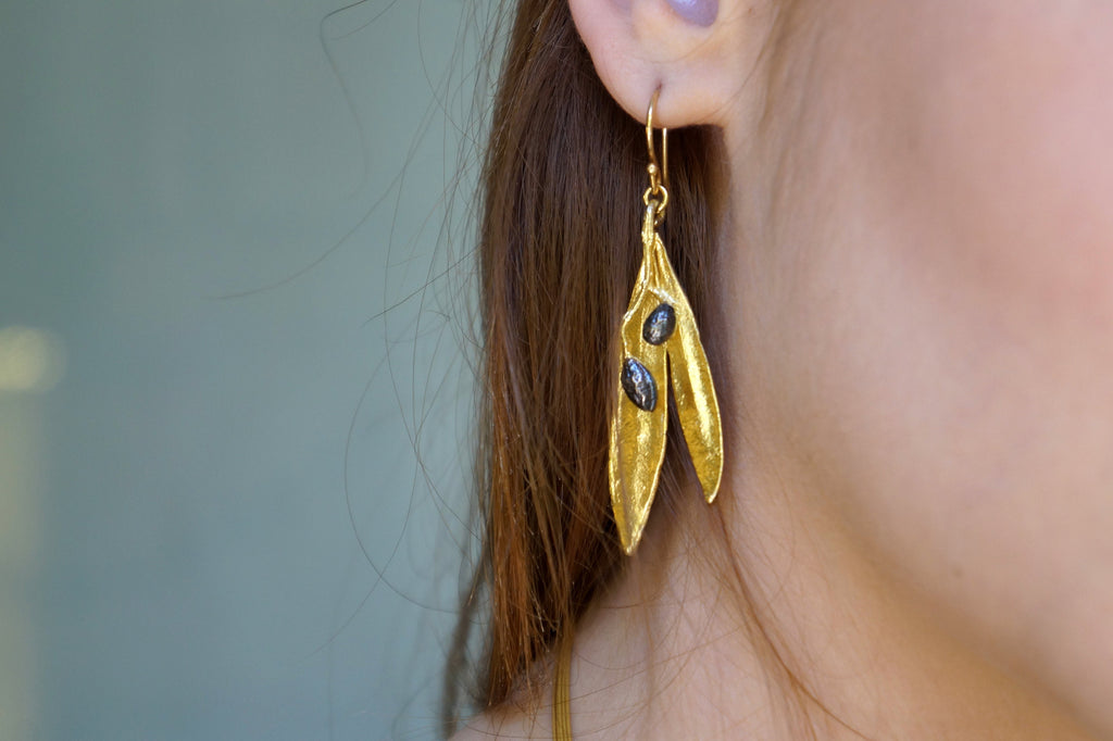 A close-up view of a person's ear wearing a pair of gold earrings with leaf-shaped designs.