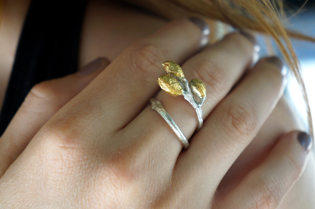 A close-up of a person's hand wearing a ring with a unique design featuring three golden flowers or leaves.