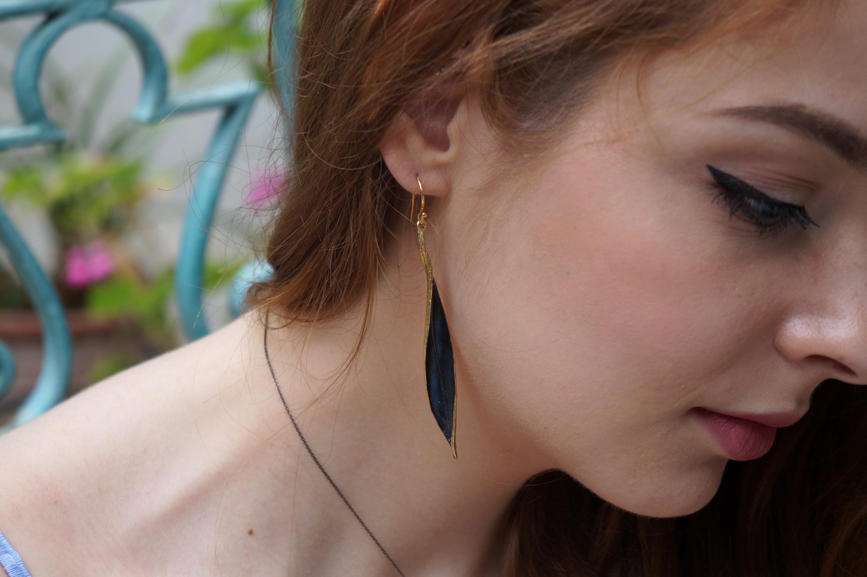 A close-up of a woman's face wearing a pair of gold earrings with a black leaf design.