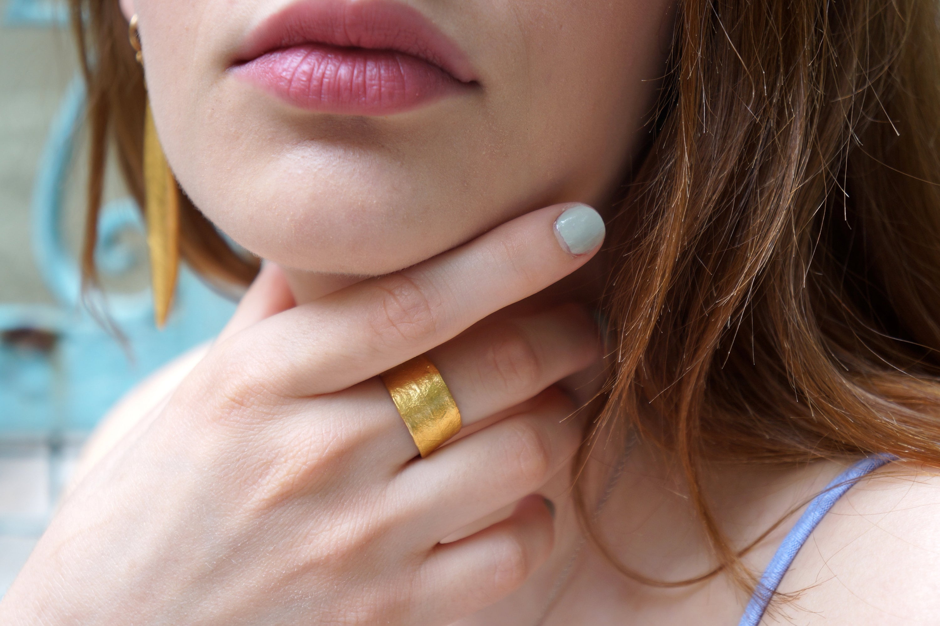 A close-up of a woman's face, focusing on her hand and finger adorned with a gold ring.