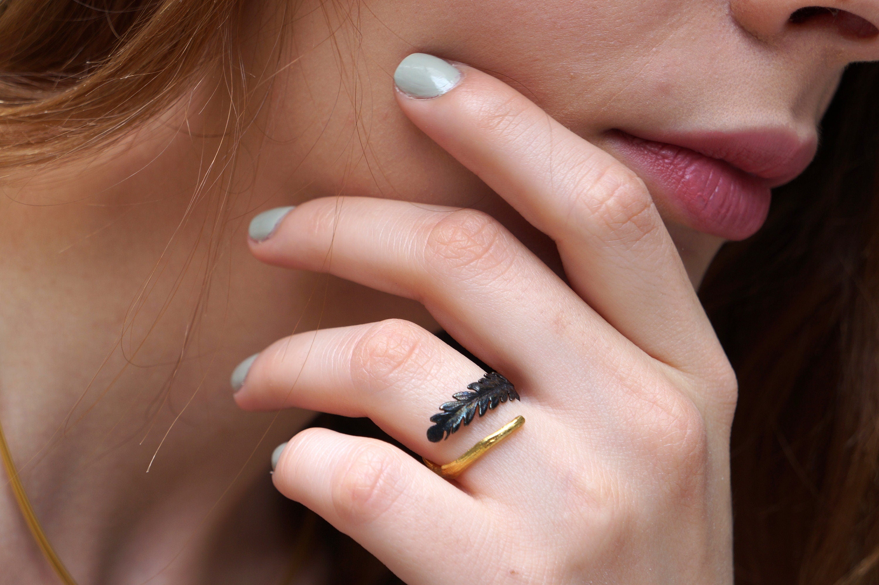 A close-up of a person's hand wearing a ring with a leaf design, resting on their thumb.