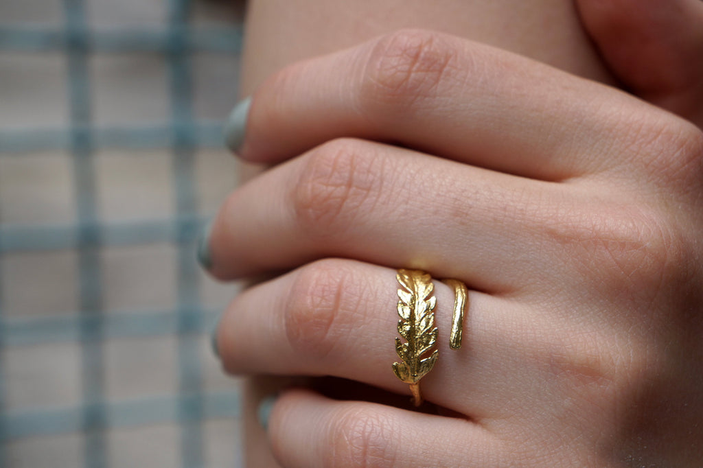 A close-up of a person's hand wearing a gold ring with a leaf-shaped design.