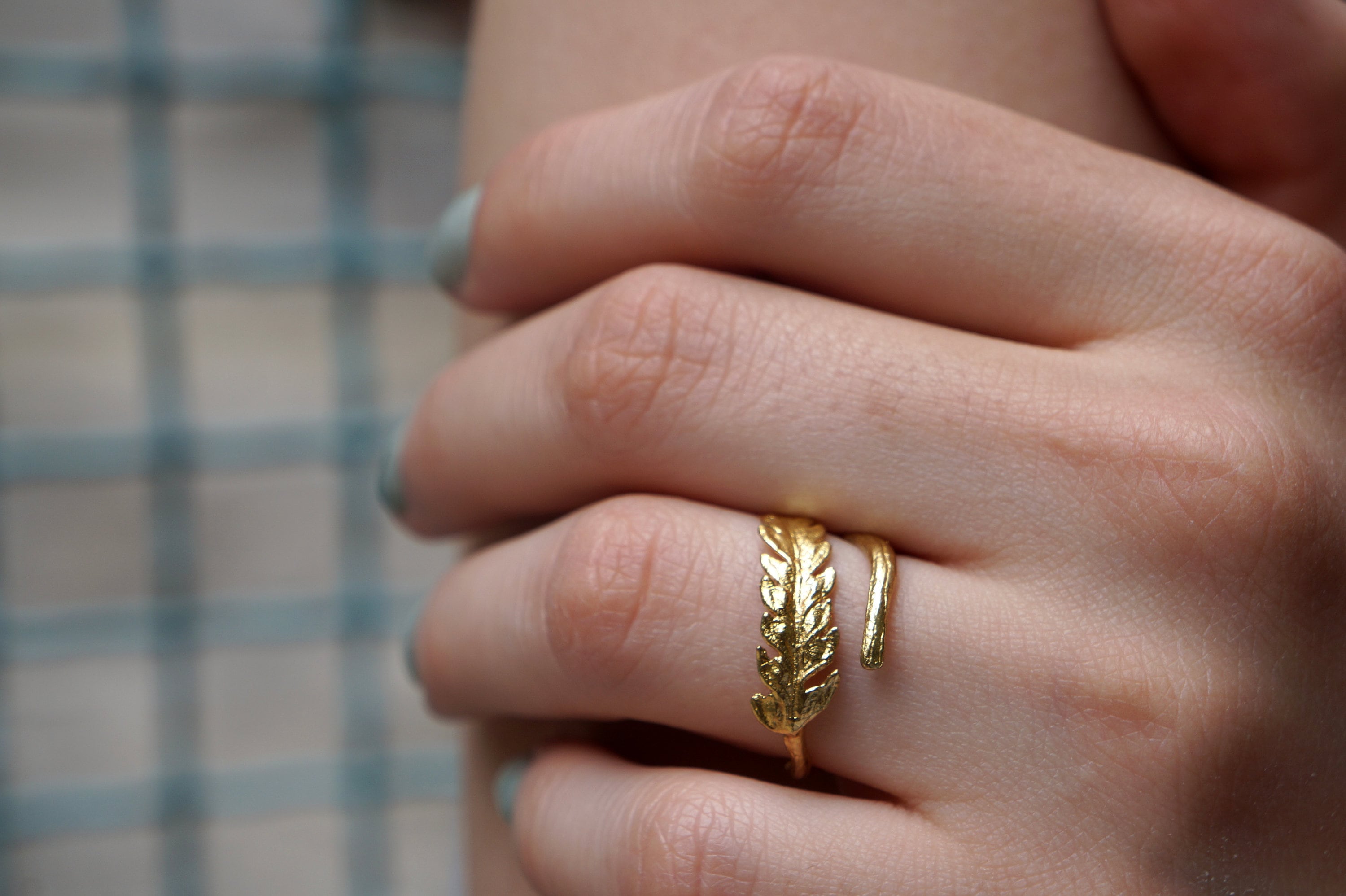 A close-up of a person's hand wearing a gold ring with a leaf-shaped design.
