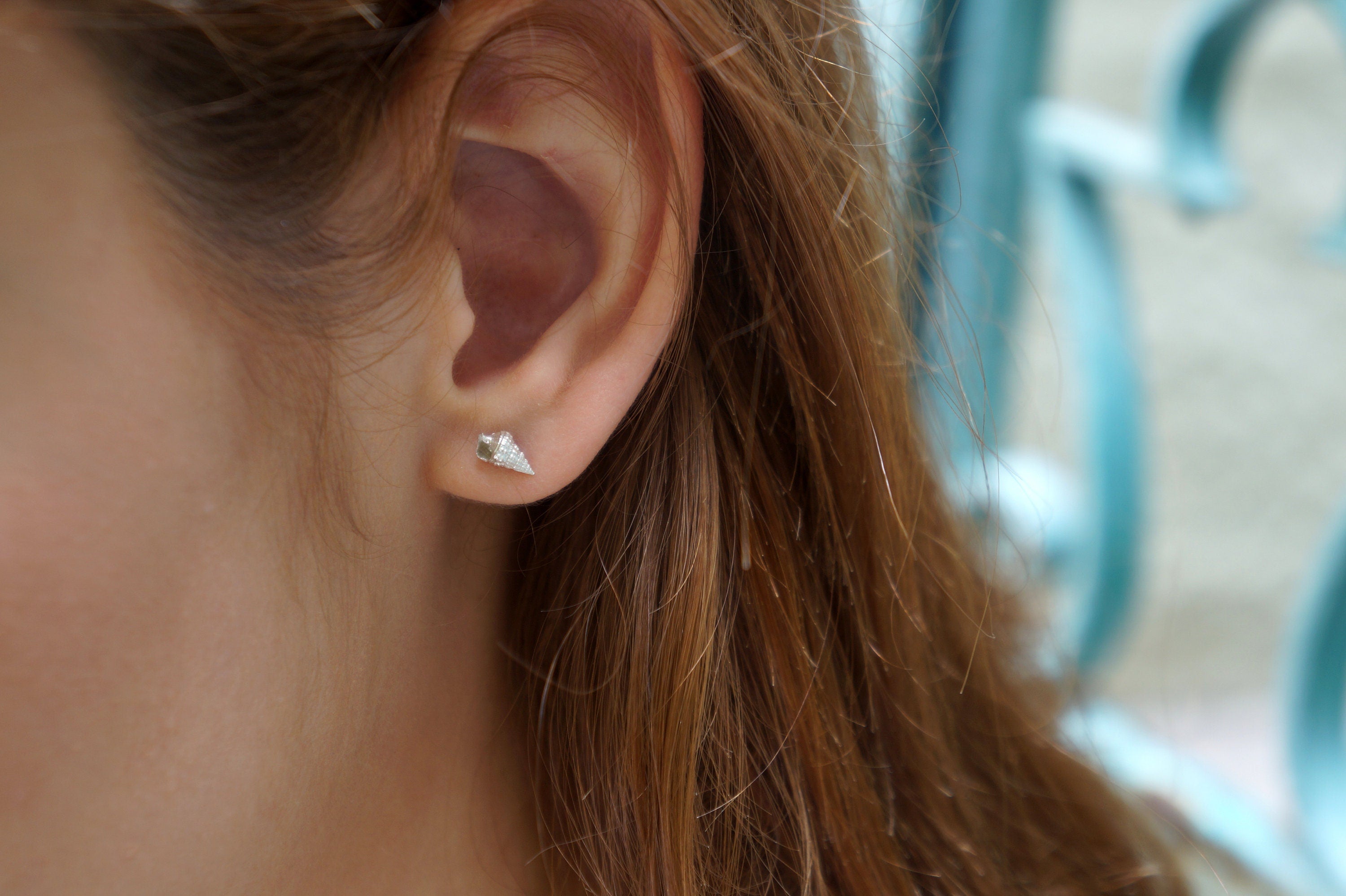 A close-up view of a person's ear adorned with a small, silver earring featuring a small, pointed design.