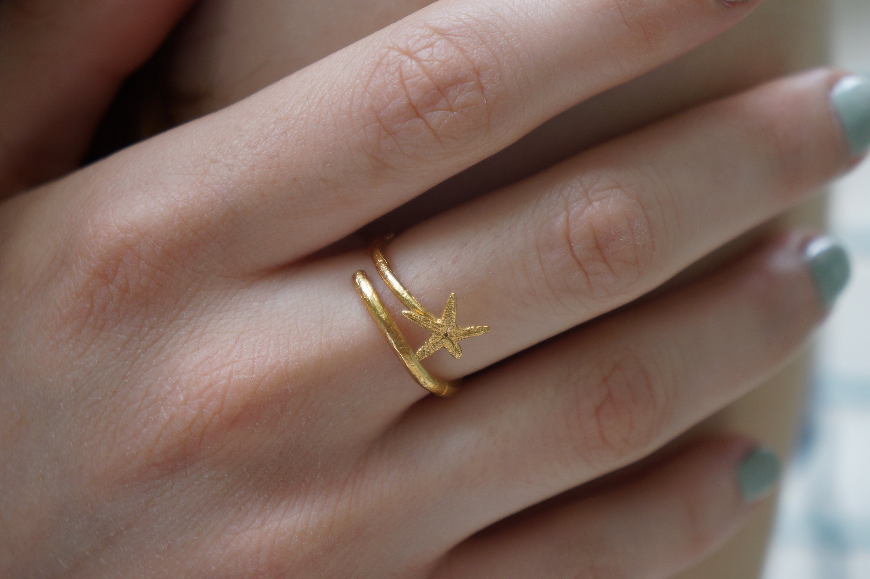 A close-up of a person's hand wearing a gold ring with a star-shaped design.