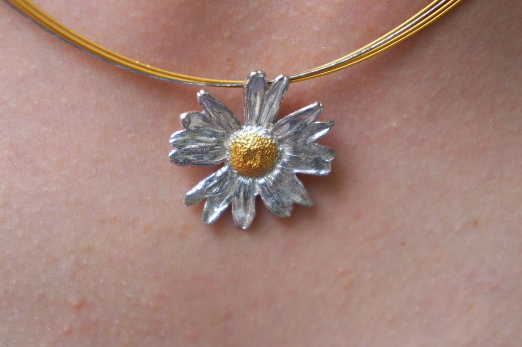 A close-up view of a delicate silver flower pendant with a gold center, hanging from a gold chain.