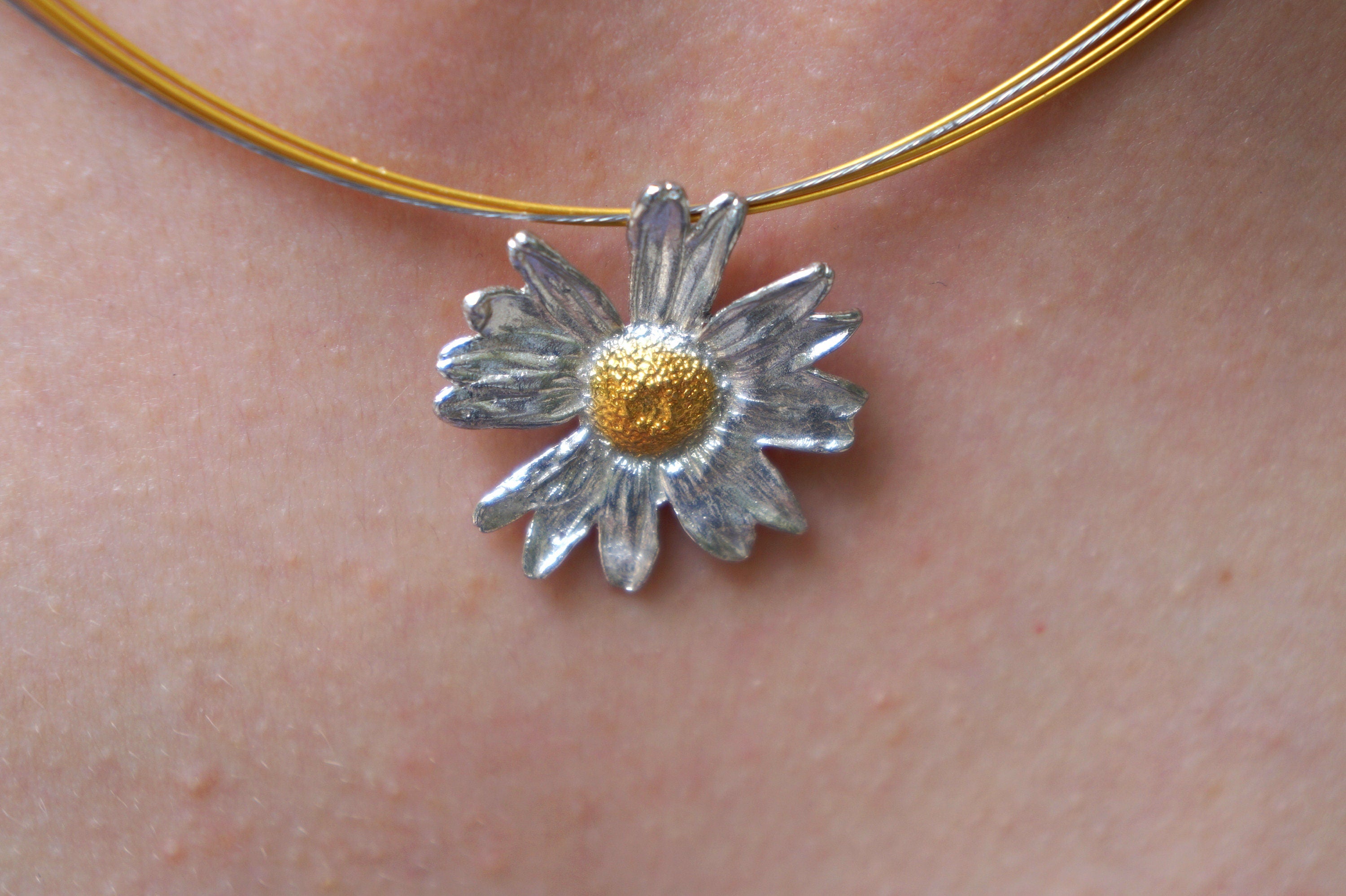 A close-up view of a delicate silver flower pendant with a gold center, hanging from a gold chain.