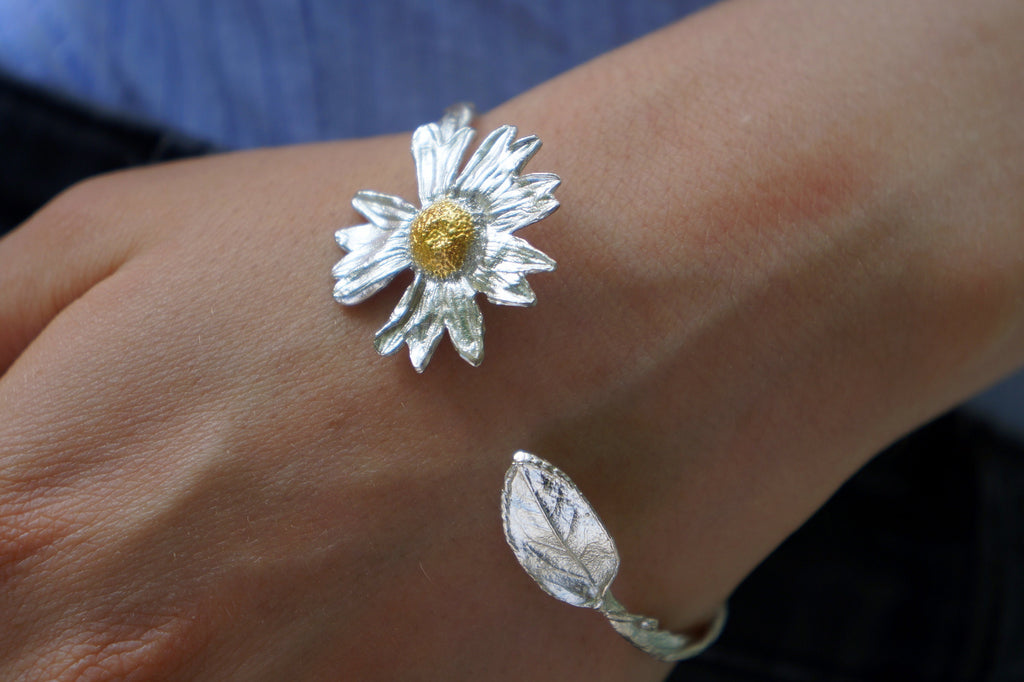 A close-up image of a person's hand wearing a silver bracelet with a large, intricately designed flower-shaped charm on the wrist.