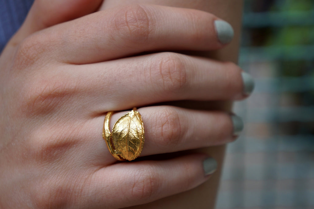 A close-up of a person's hand wearing a gold leaf ring on the ring finger.