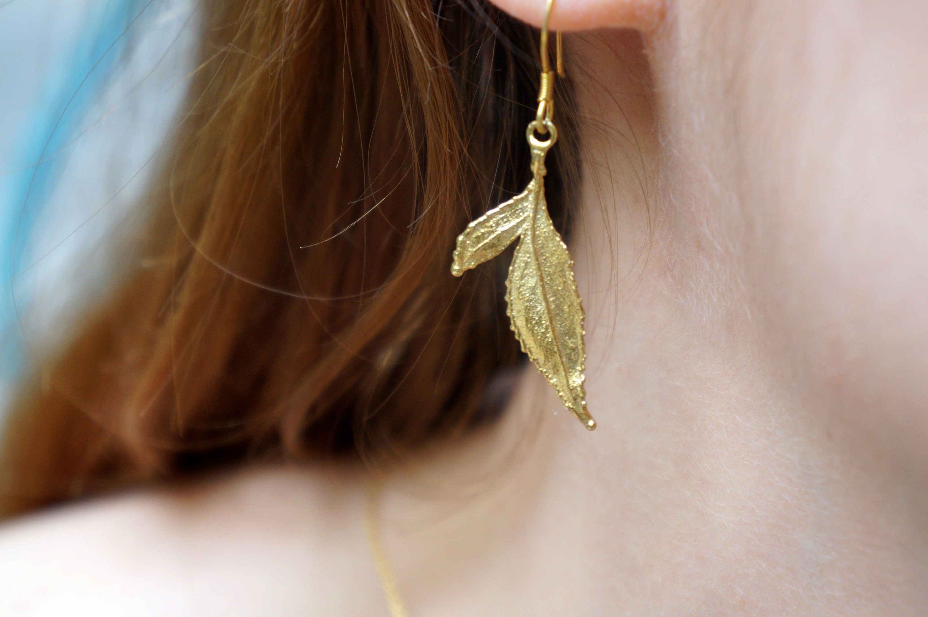 A close-up view of a person's ear wearing a gold leaf earring.