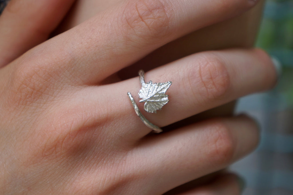 A close-up image of a person's hand wearing a silver ring with a leaf design.