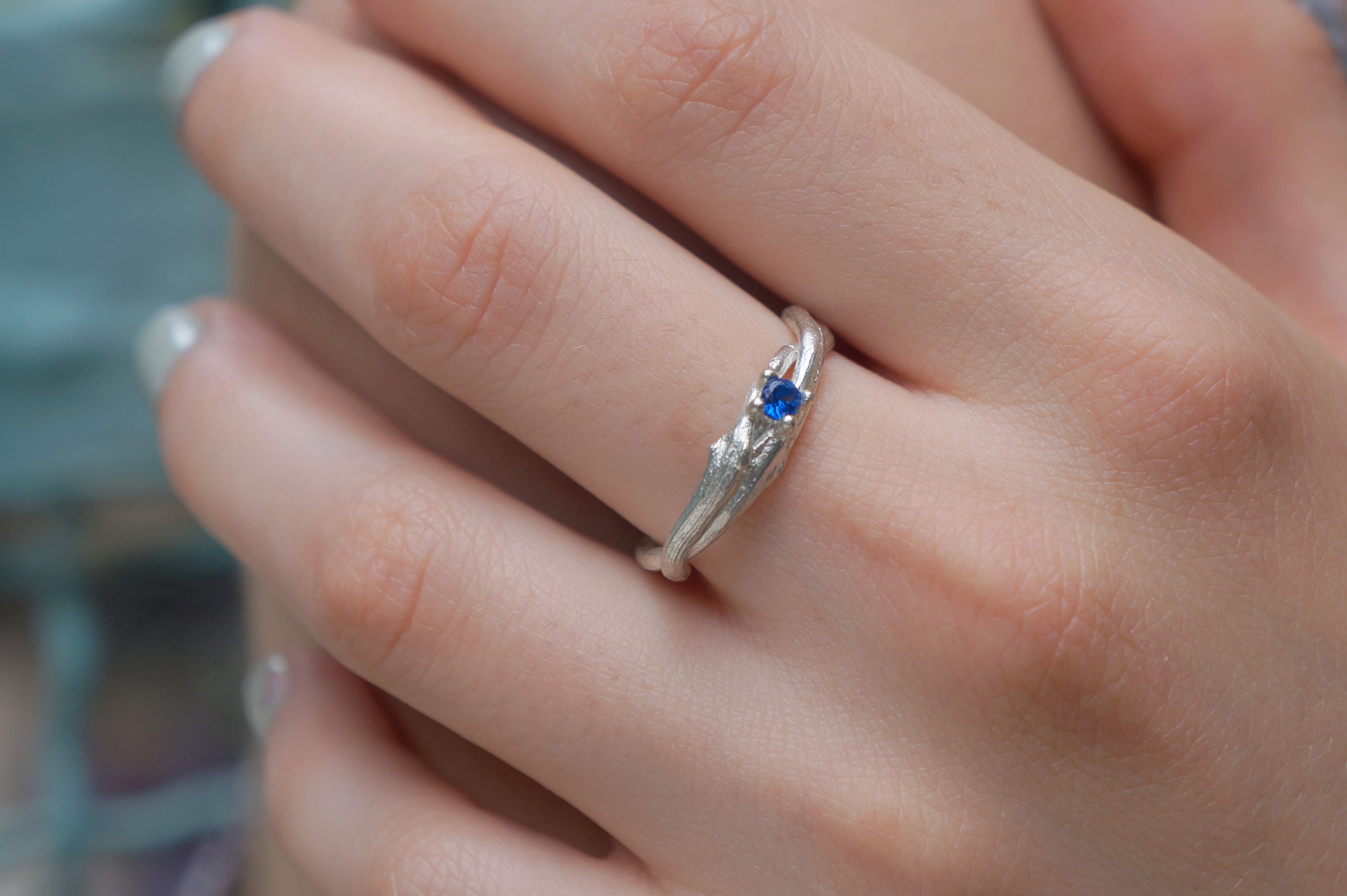 A close-up image of a person's hand wearing a silver ring with a blue gemstone.