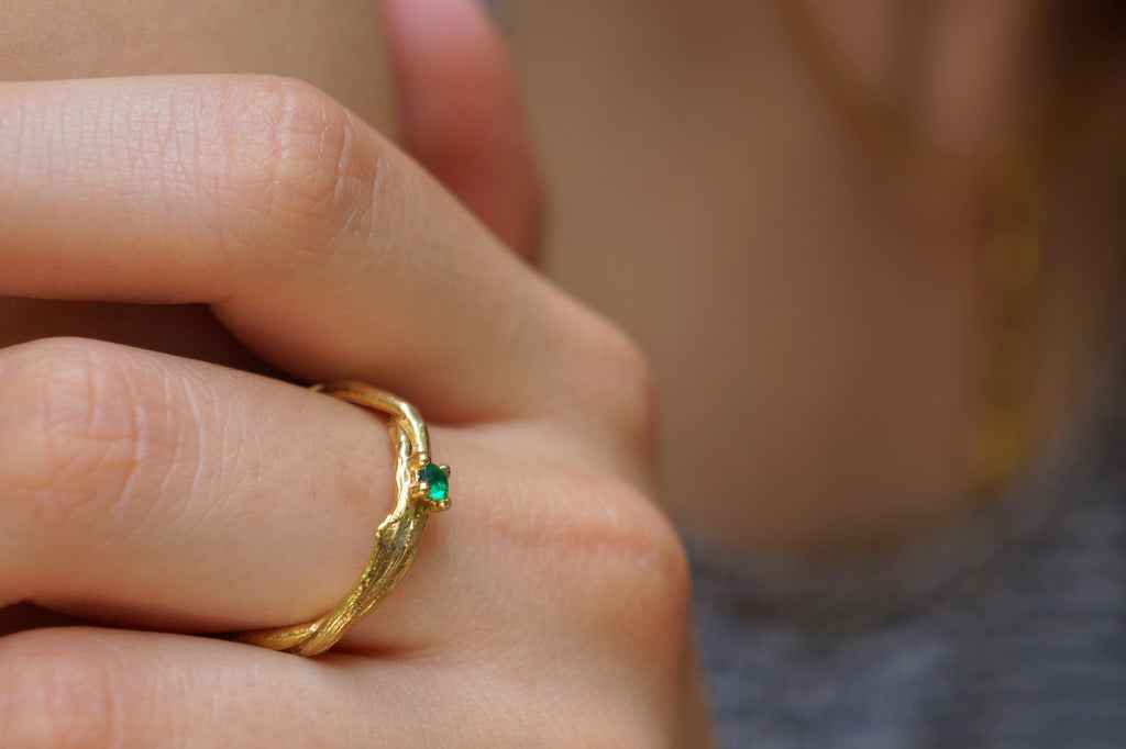 A close-up of a person's hand wearing a gold ring with a green gemstone.
