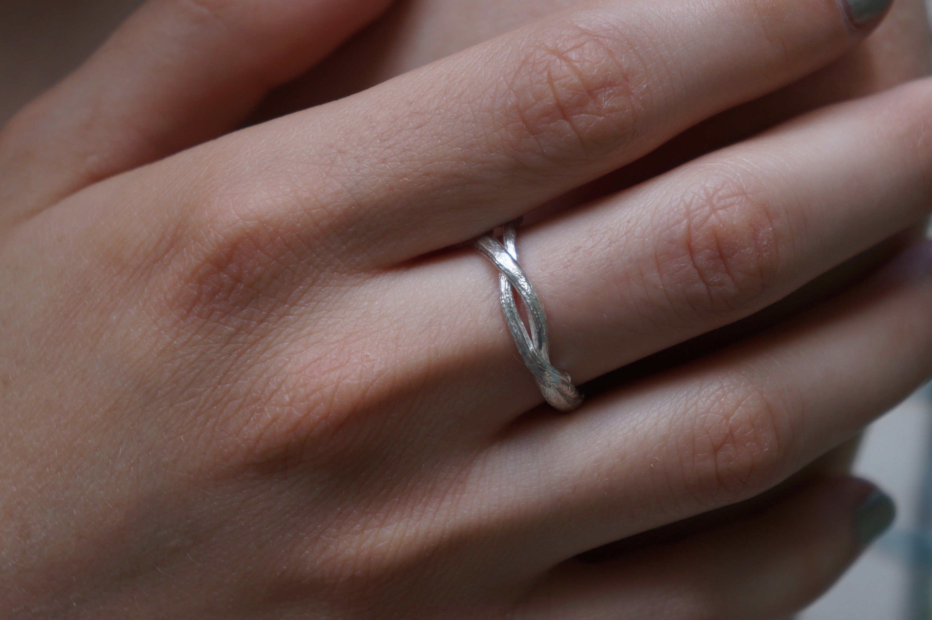 A close-up view of a person's hand wearing a silver ring on the ring finger.