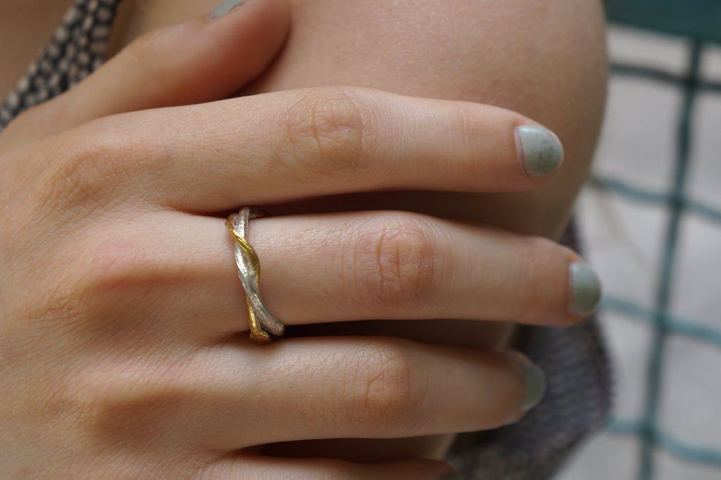 A close-up of a person's hand wearing a gold and silver ring on the ring finger.
